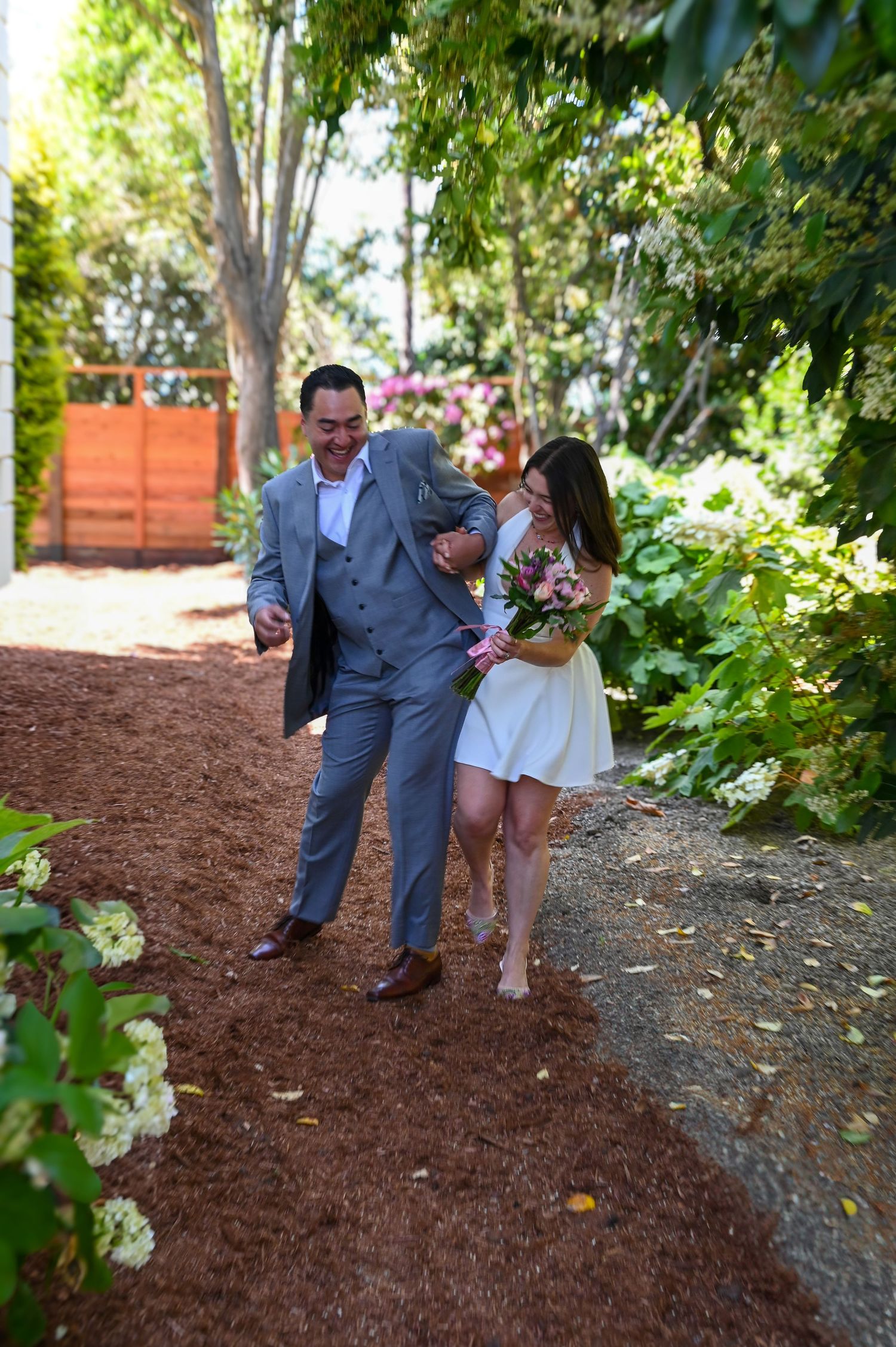 A couple walking and laughing together on a garden path surrounded by greenery.