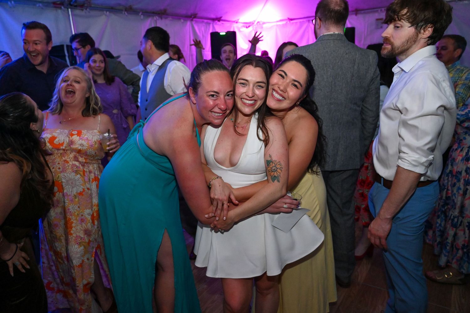 Wedding reception dance floor lit with purple and pink lighting as guests celebrate.