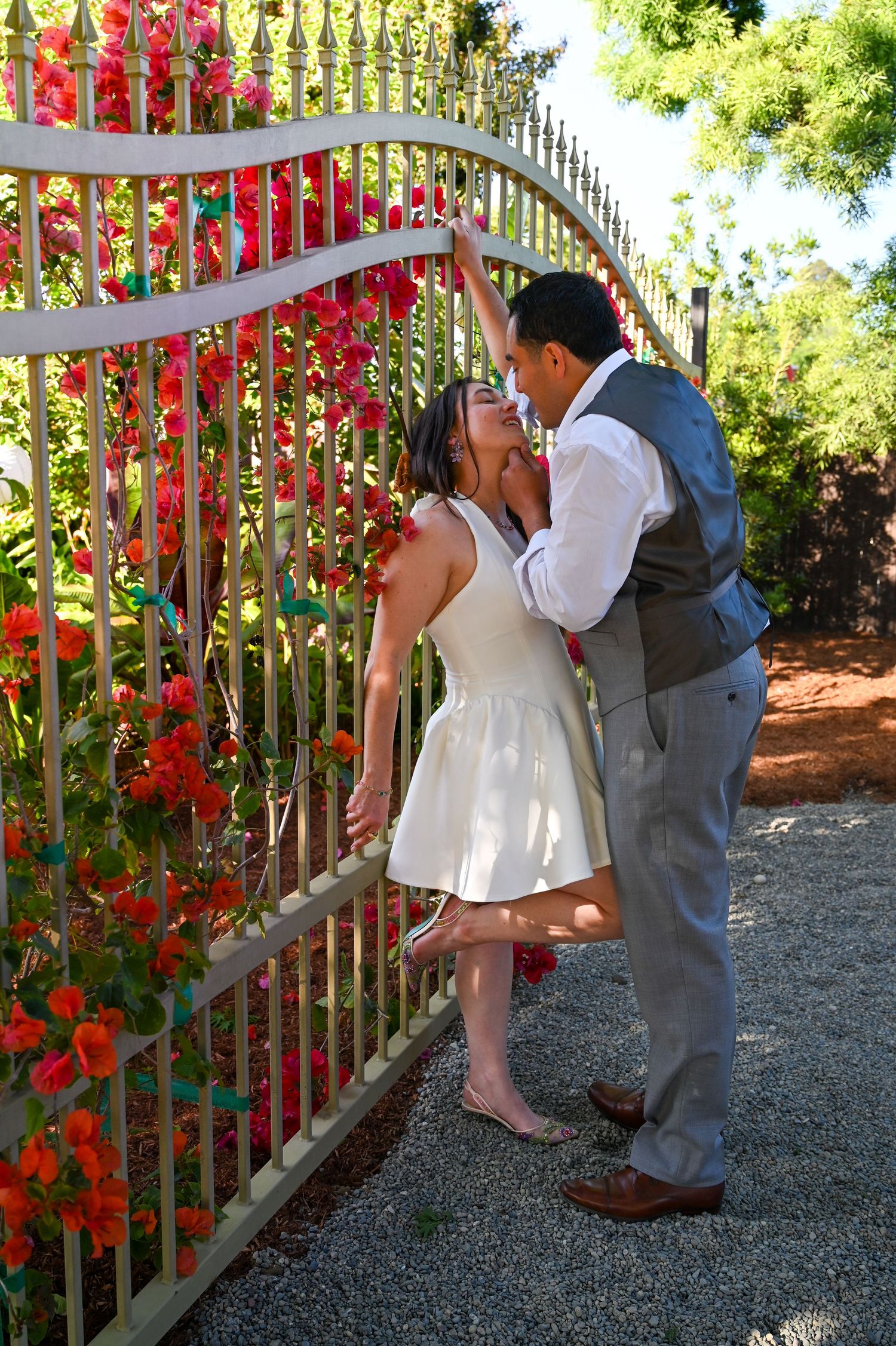 A romantic moment captured near a fence adorned with vibrant red climbing flowers.