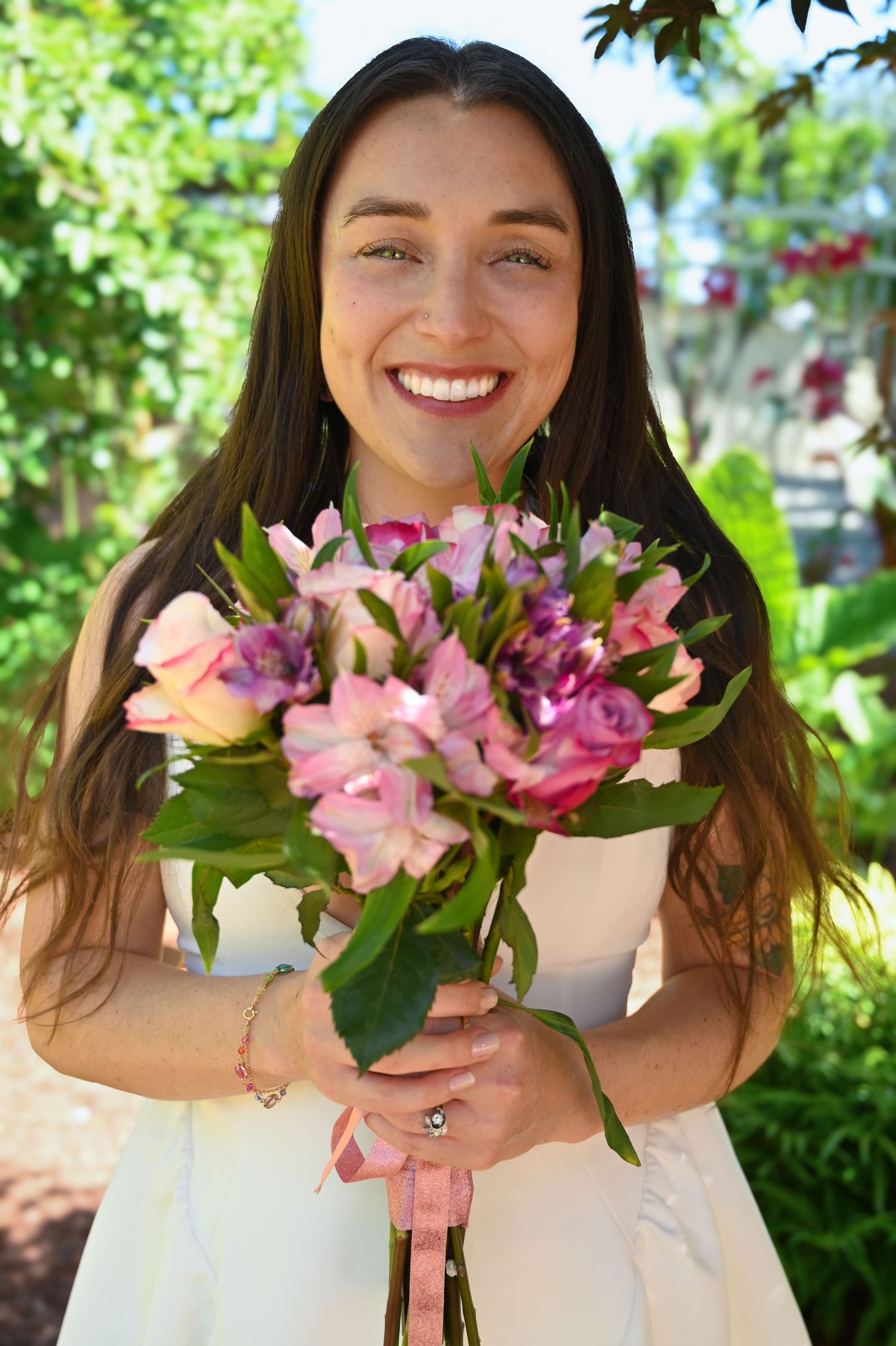 A cheerful person in white holding a vibrant pink and peach floral bouquet outdoors.