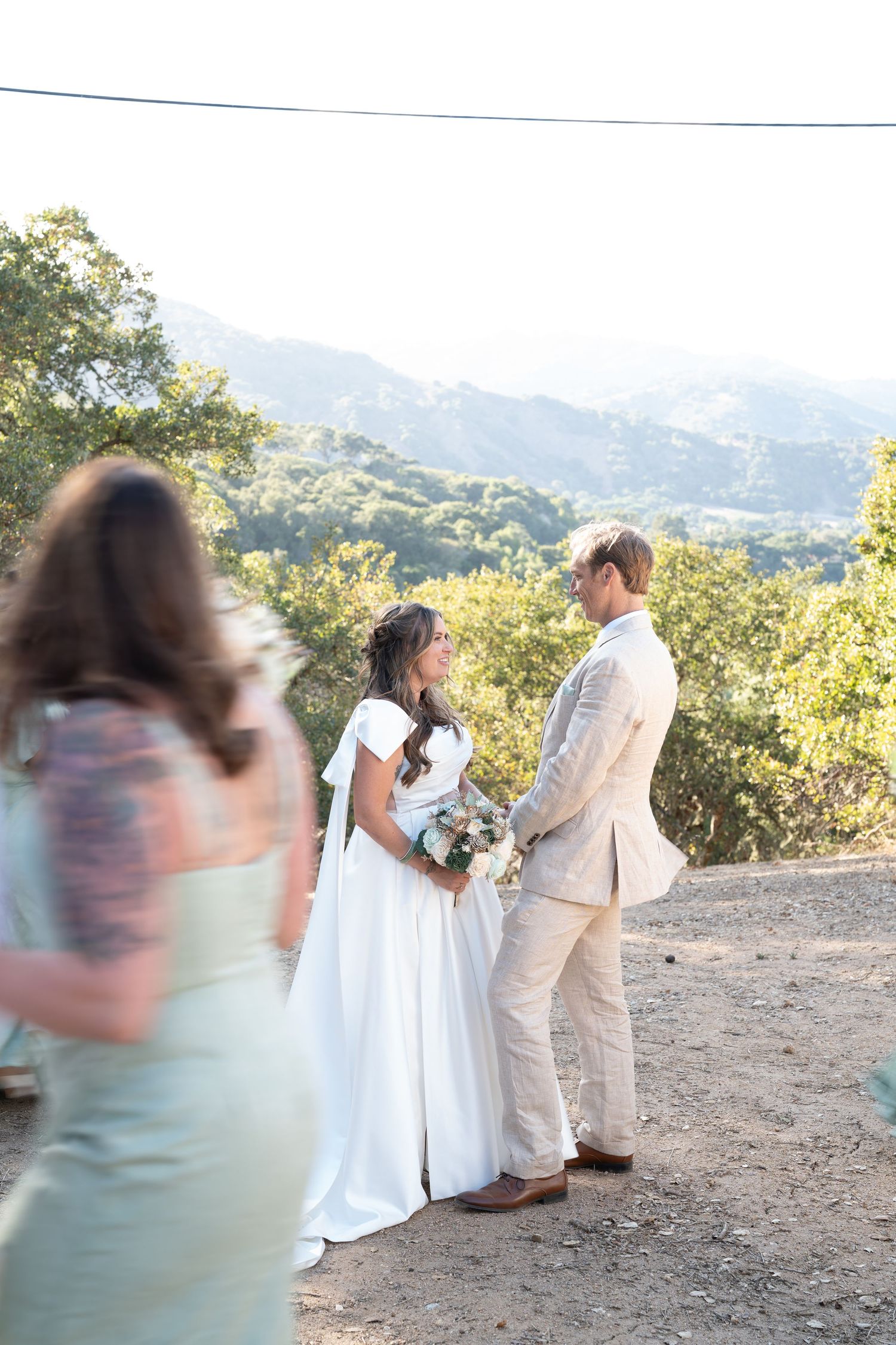 A couple exchanges vows during an outdoor mountain wedding ceremony with green hills and trees in the background.
