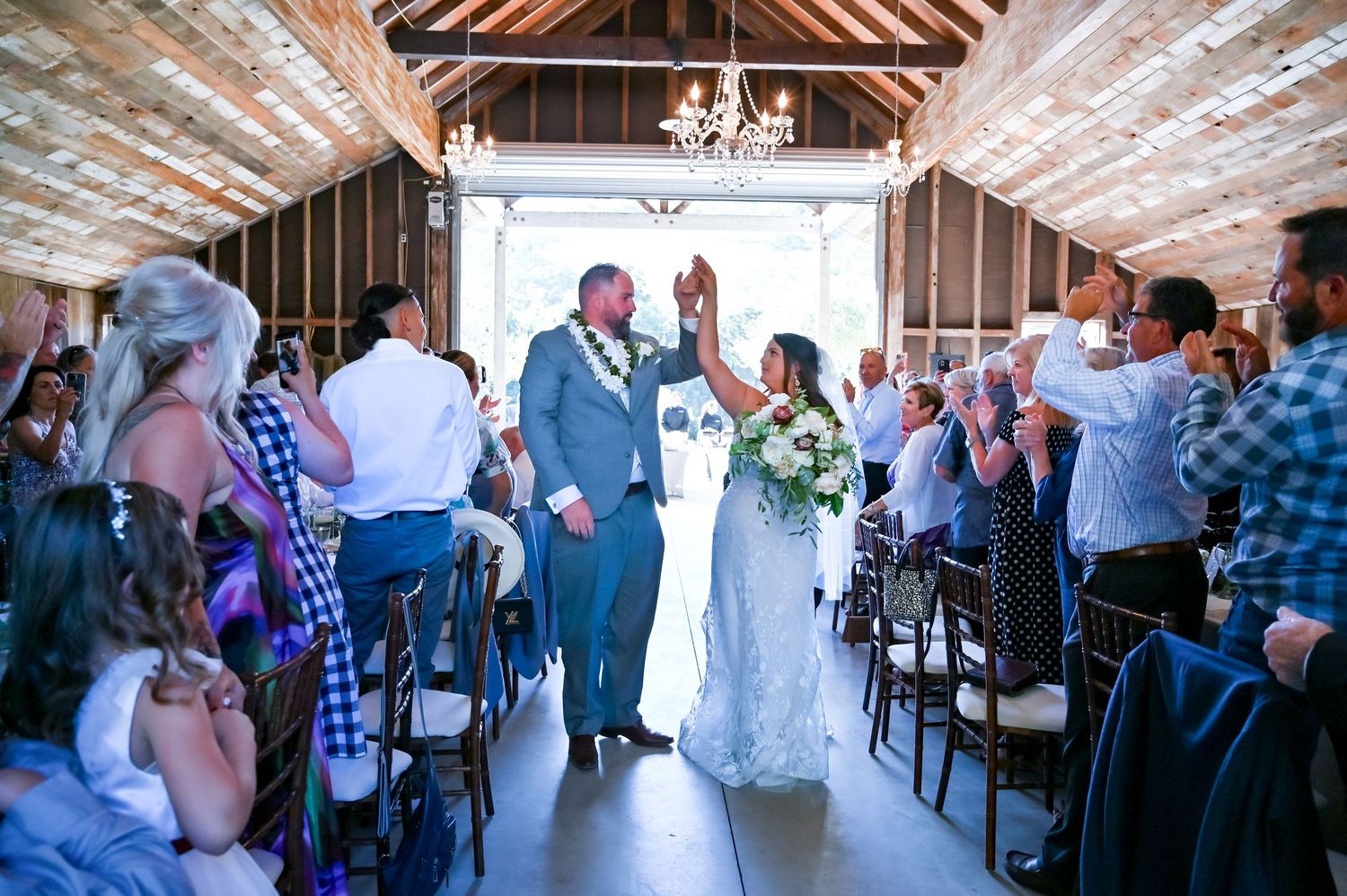 Wedding guests celebrating in a rustic reception hall with wooden ceiling beams.