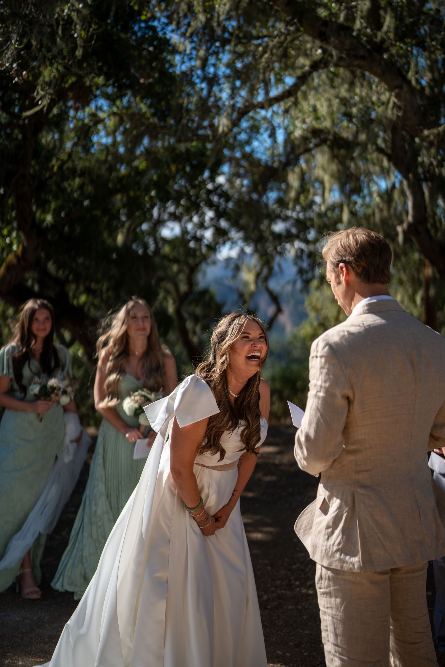 A couple shares joyful candid moments during an outdoor wedding photoshoot against a natural backdrop.