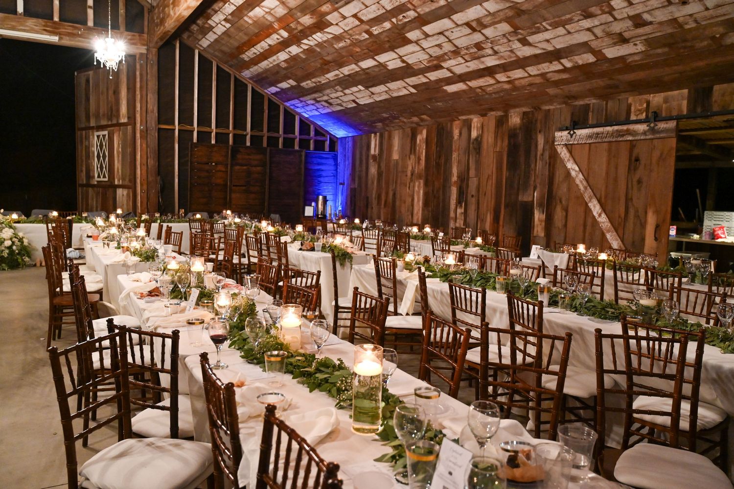 Elegant barn wedding reception setup with long tables and romantic lighting.