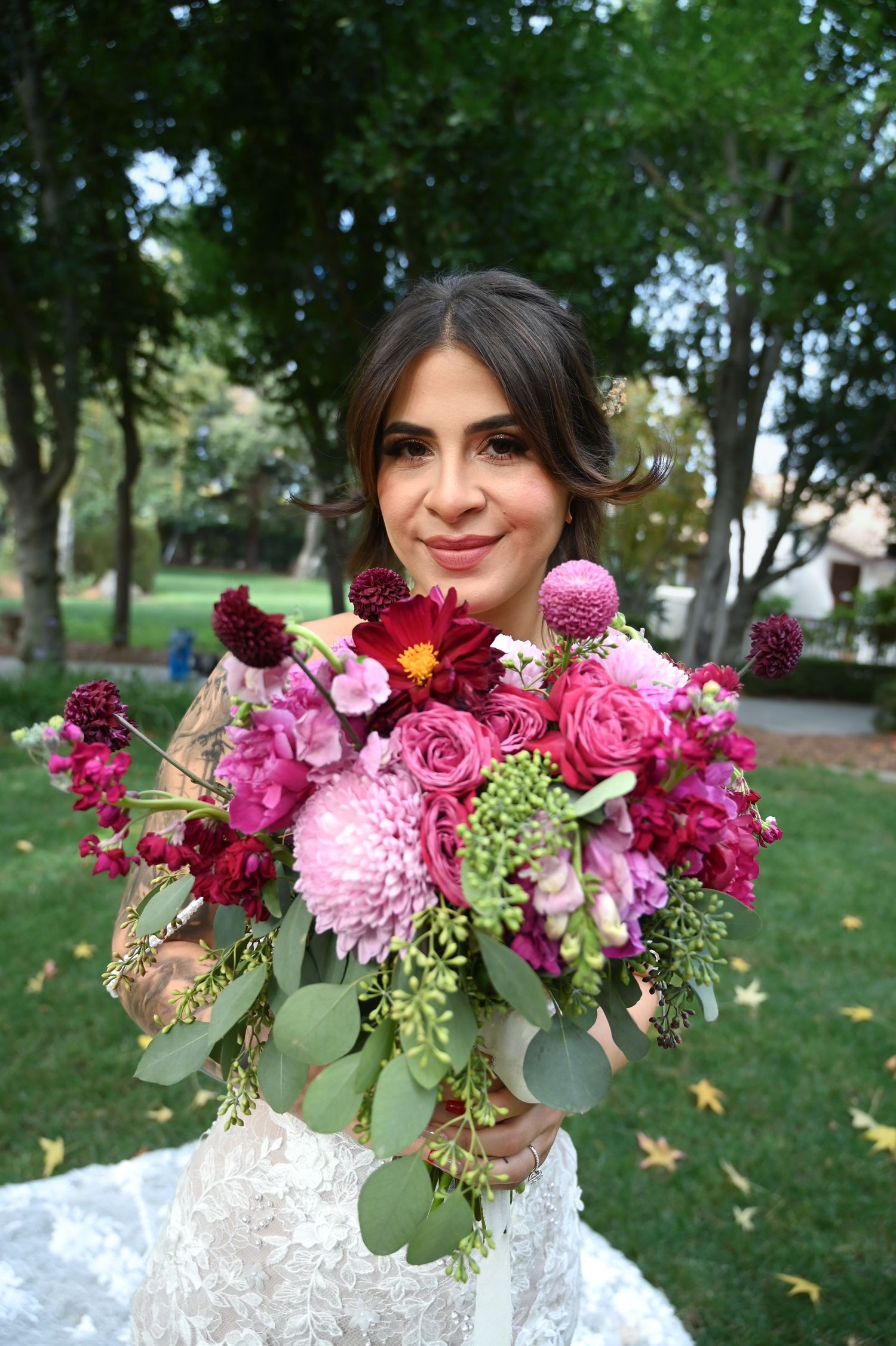 A romantic bridal bouquet features pink roses, burgundy dahlias, and eucalyptus against a garden backdrop.