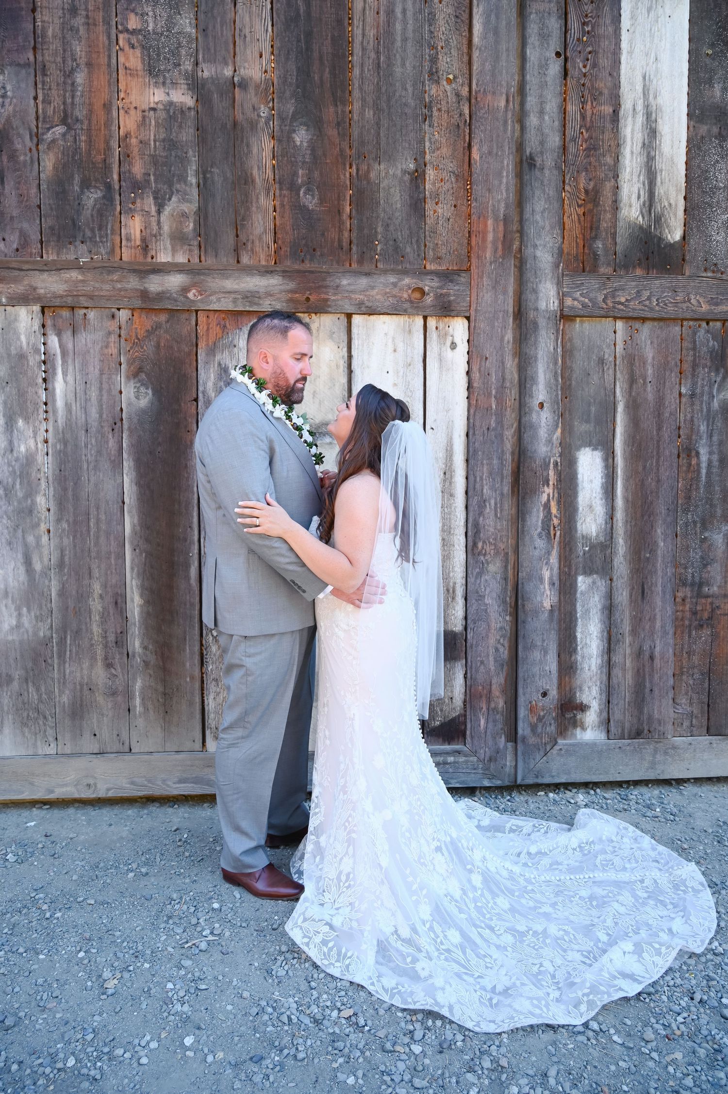 Emotional first look moment captured against weathered wooden barn wall.