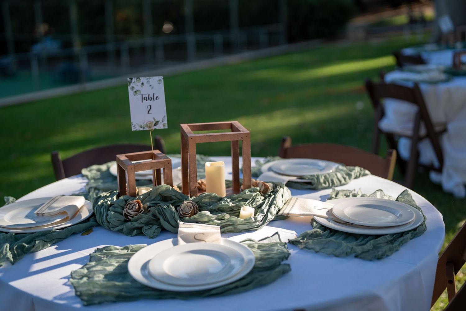 Elegant outdoor wedding reception table settings with wooden chairs and white linens.