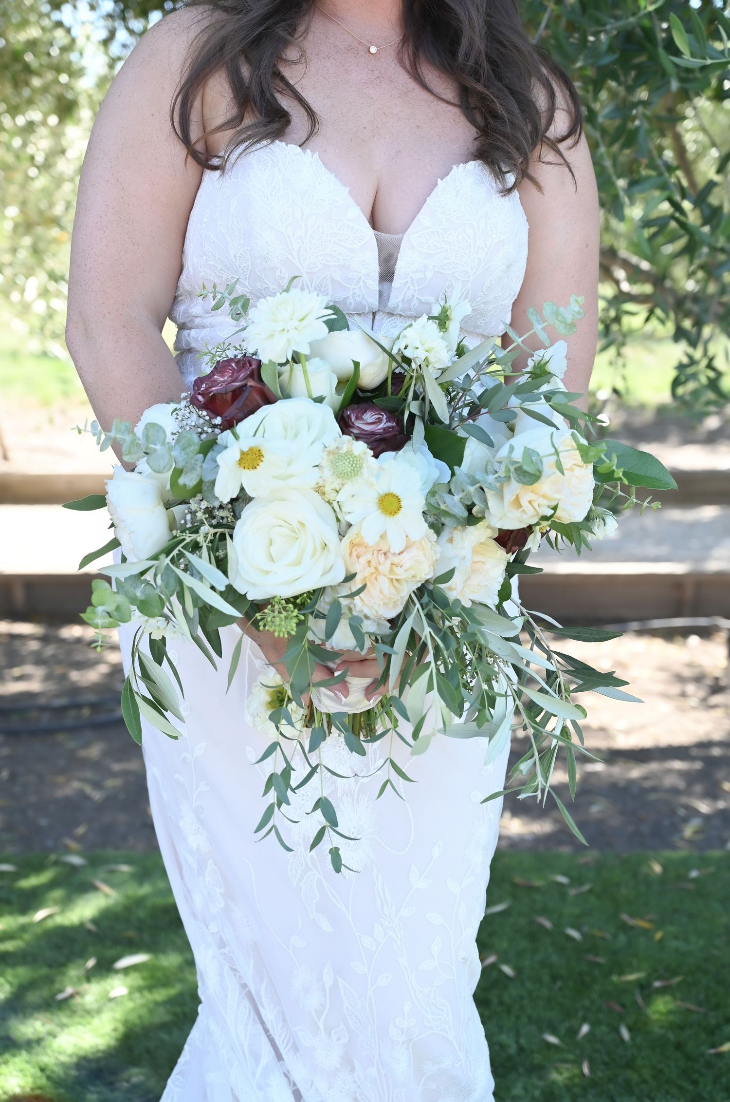 Close up of bridal bouquet with white roses and mixed flowers against lace wedding dress.