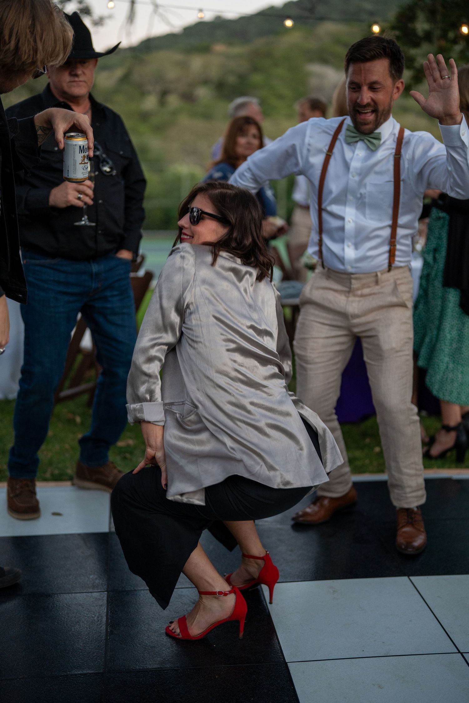 A sequence of dance moves showing someone in a gray shirt and red shoes spinning on a black dance floor at an outdoor event.