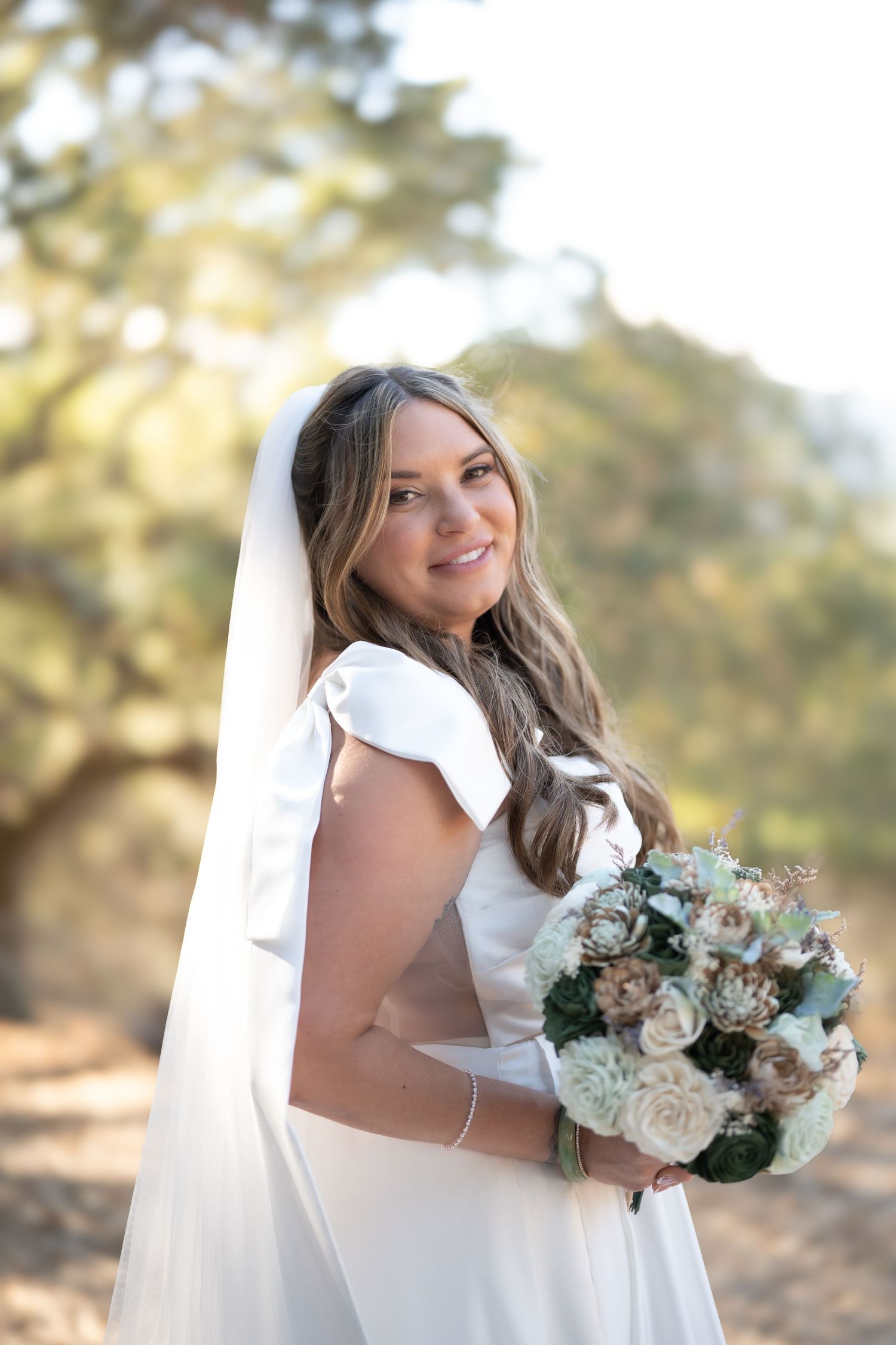 Carmel Valley Wedding Bride in white wedding dress holding elegant bouquet of white roses and blue flowers poses in natural outdoor setting.