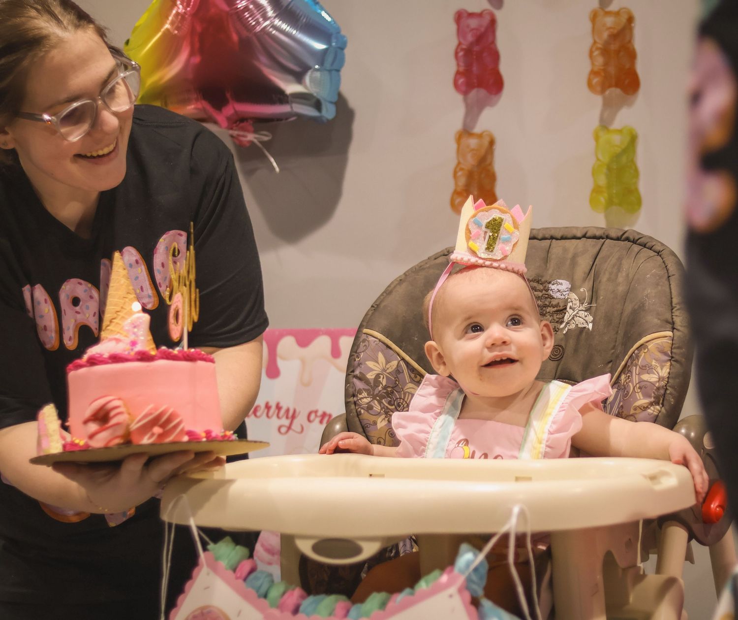 One year old girl looks up at dad as mom brings her the smash cake and lovingly looks at baby