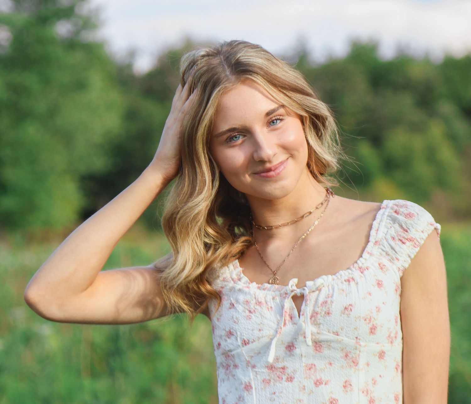 Blonde female senior gently smiling in a field while she plays with her hair
