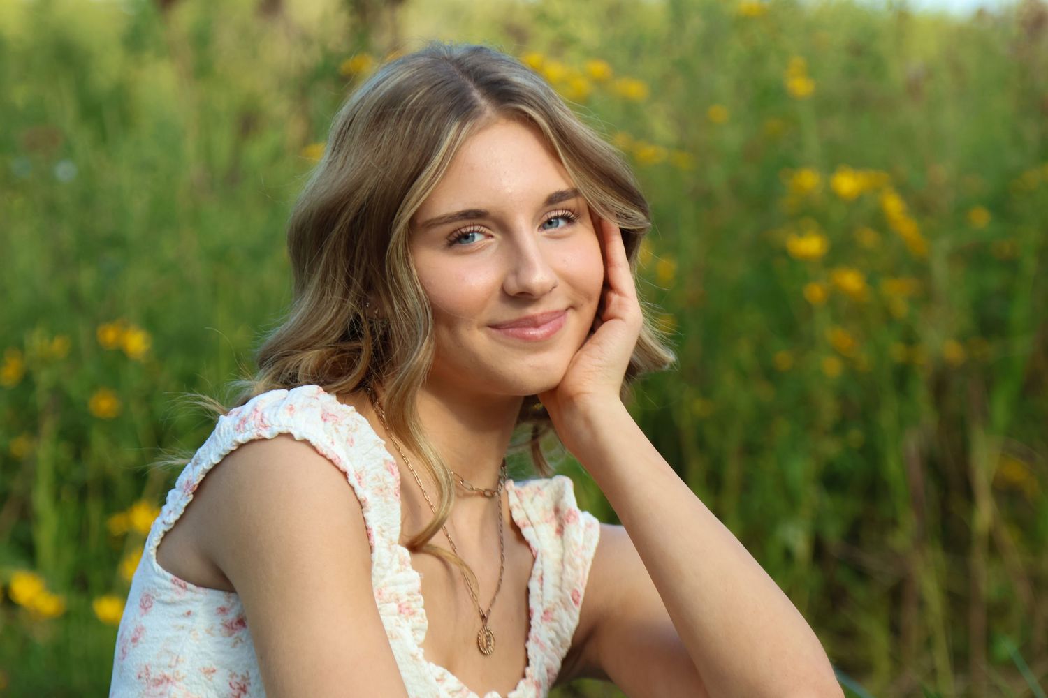 Senior girl smiling while resting her head in a her hand with little yellow flowers all around her photo taken at Goodnow Grove