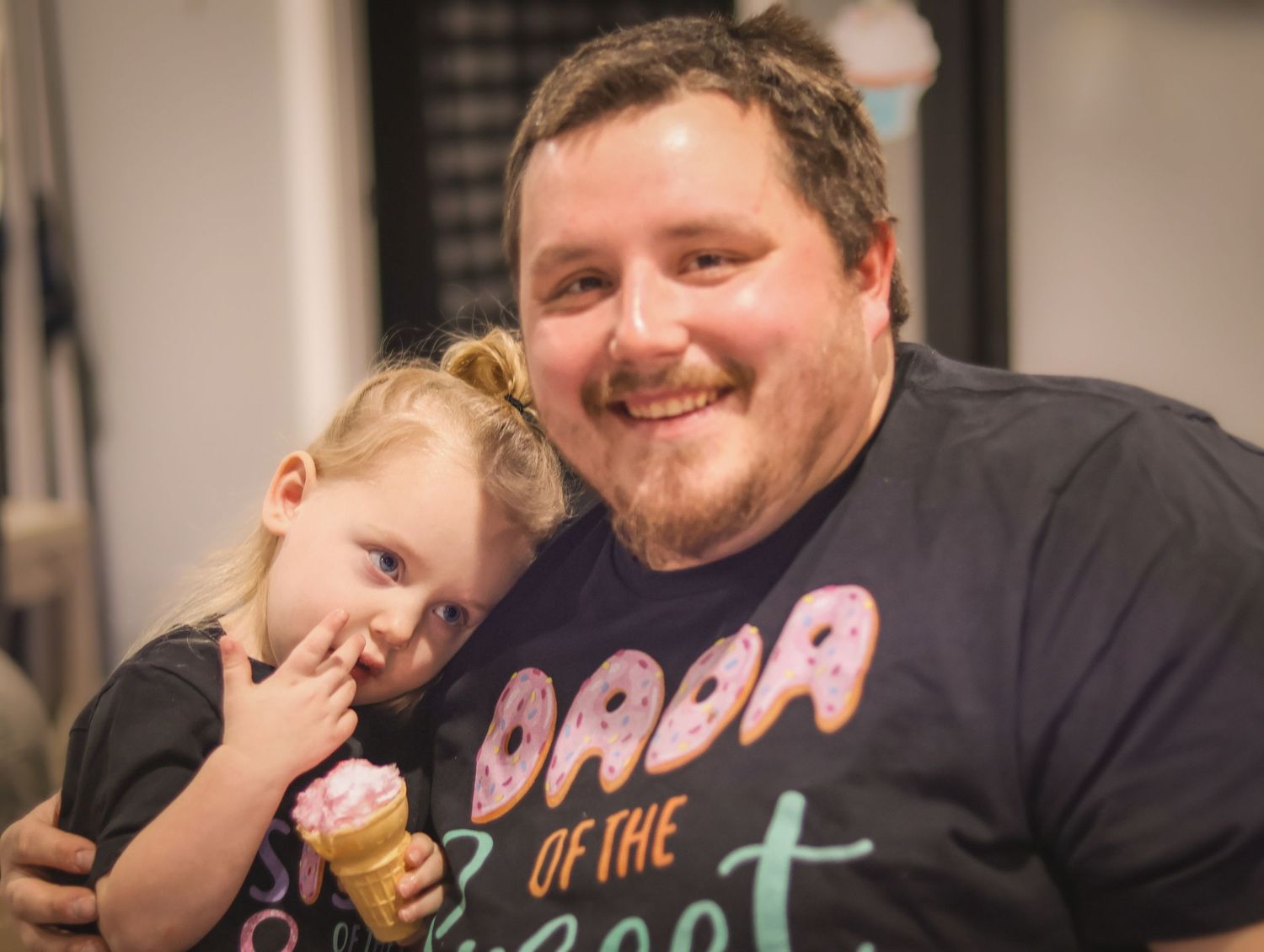 Dad and big sister smile at one year old sisters birthday party as they wear matching birthday shirts