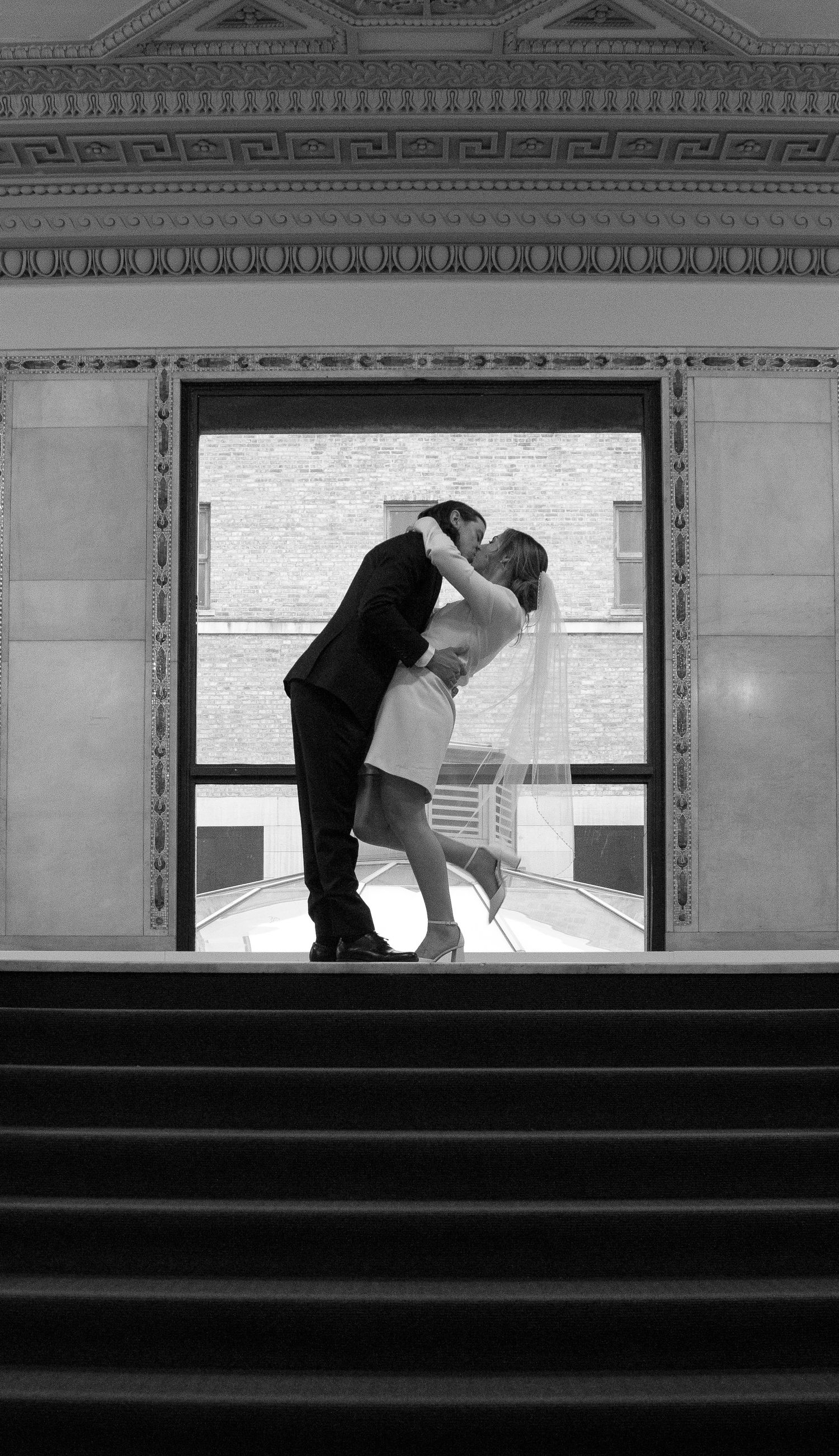 Bride and groom kiss at the top of the stairs while bride pops her knee is very cute pose