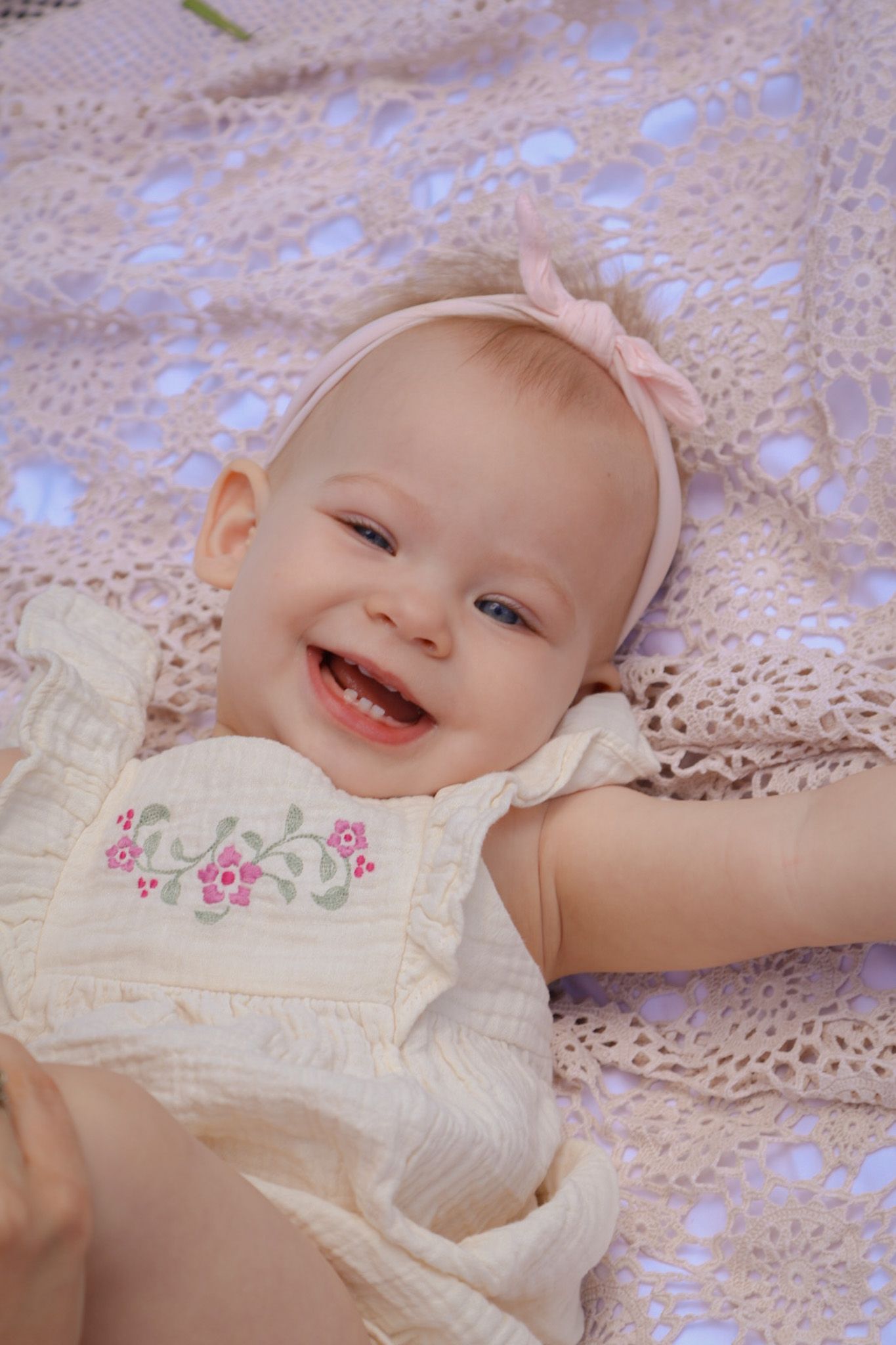 Baby girl is laying back on crochet blanket and smiling with the sunlight on her in cedar lake In