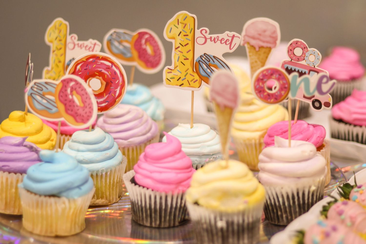 Tray covered with pastel and pink colored birthday cupcakes with donut and sprinkle cake toppers for first birthday party