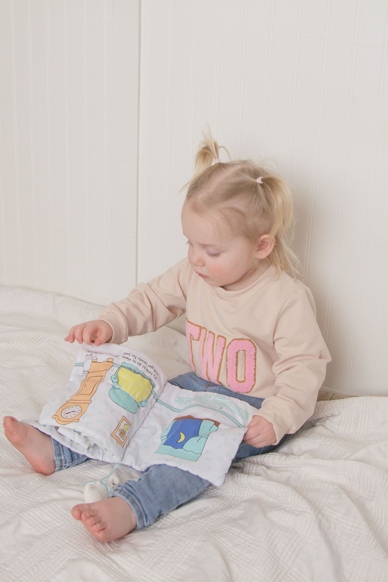 Toddler girl sitting on a bed reading a book during an in home lifestyle family photography session in Crete Illinois