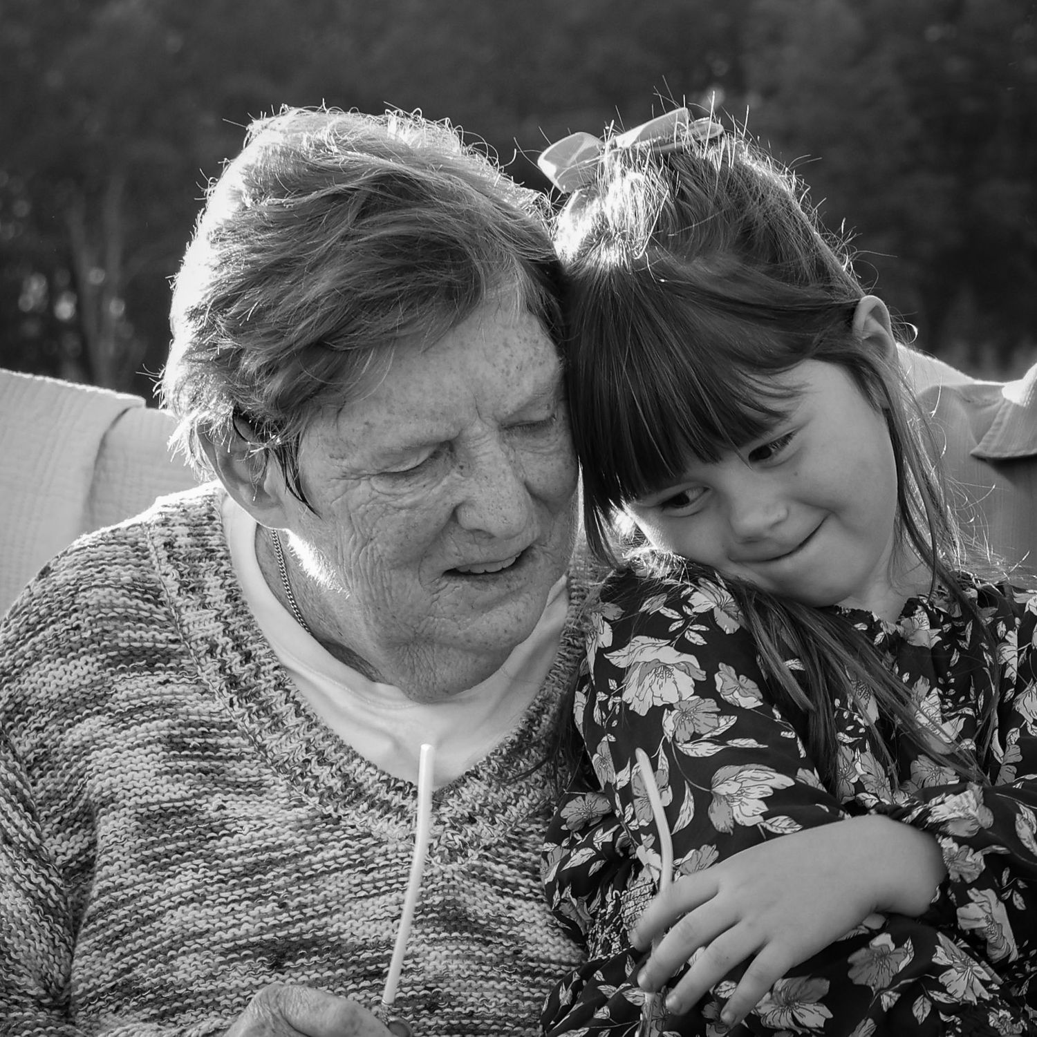Grandmother holds her granddaughter close and they lean into each other and snuggle up black and white