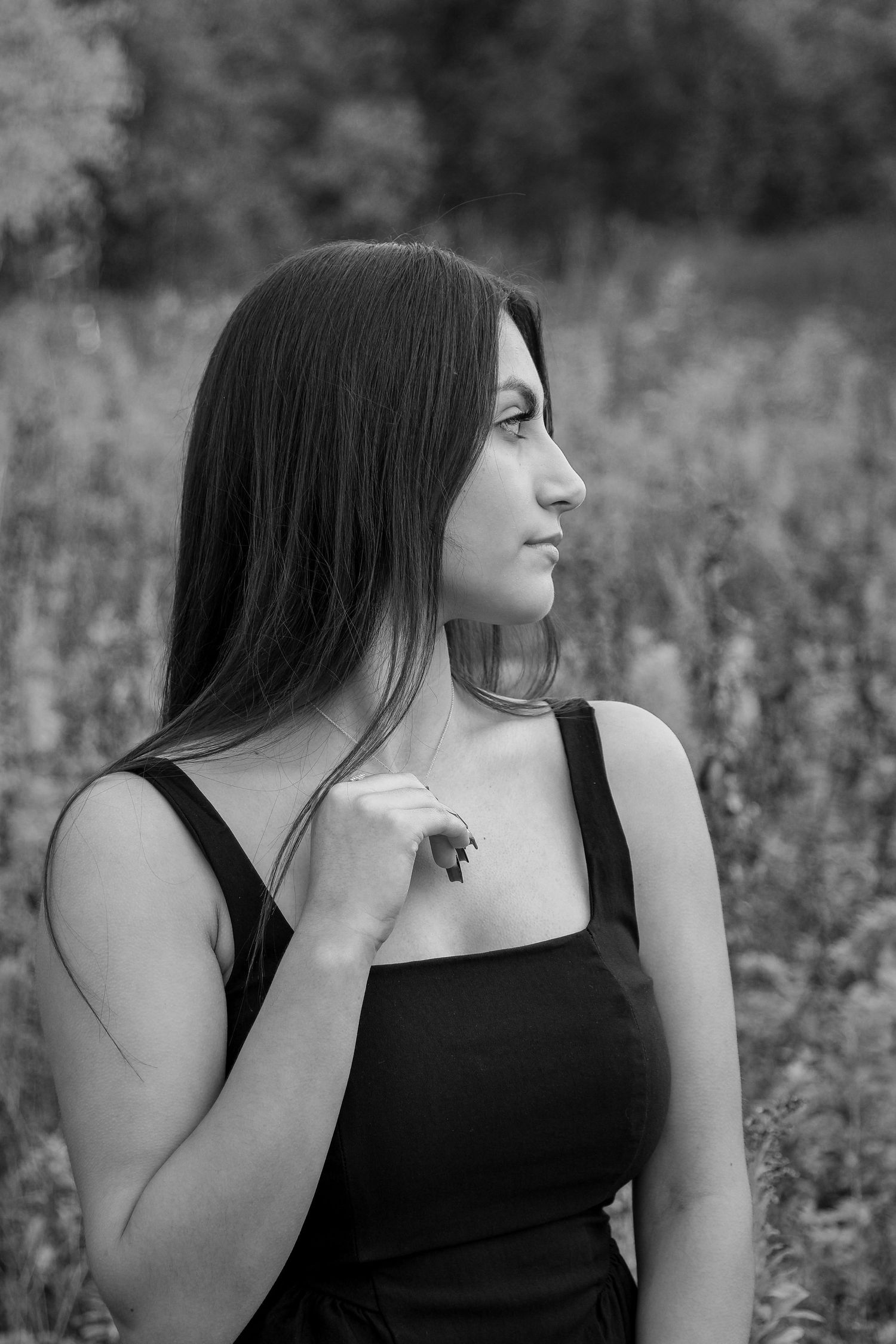Brunette senior girl looking over shoulder while she is in a field. photo in black and white