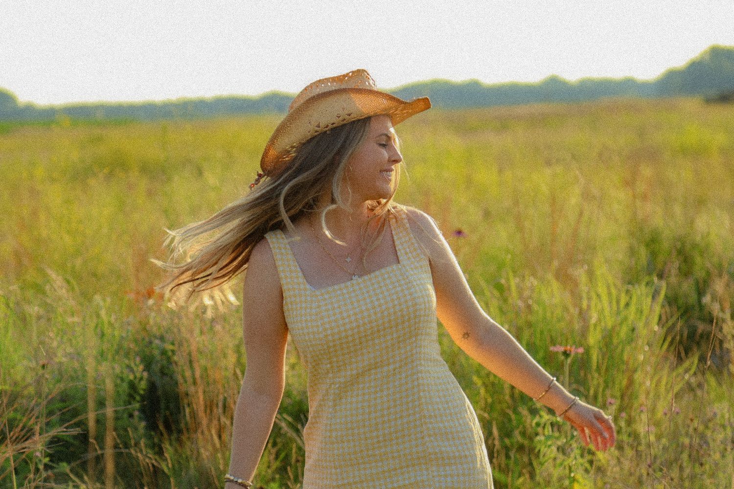 Woman in a yellow dress and cowboy hat twirling thru a sunlit field during golden hour photos