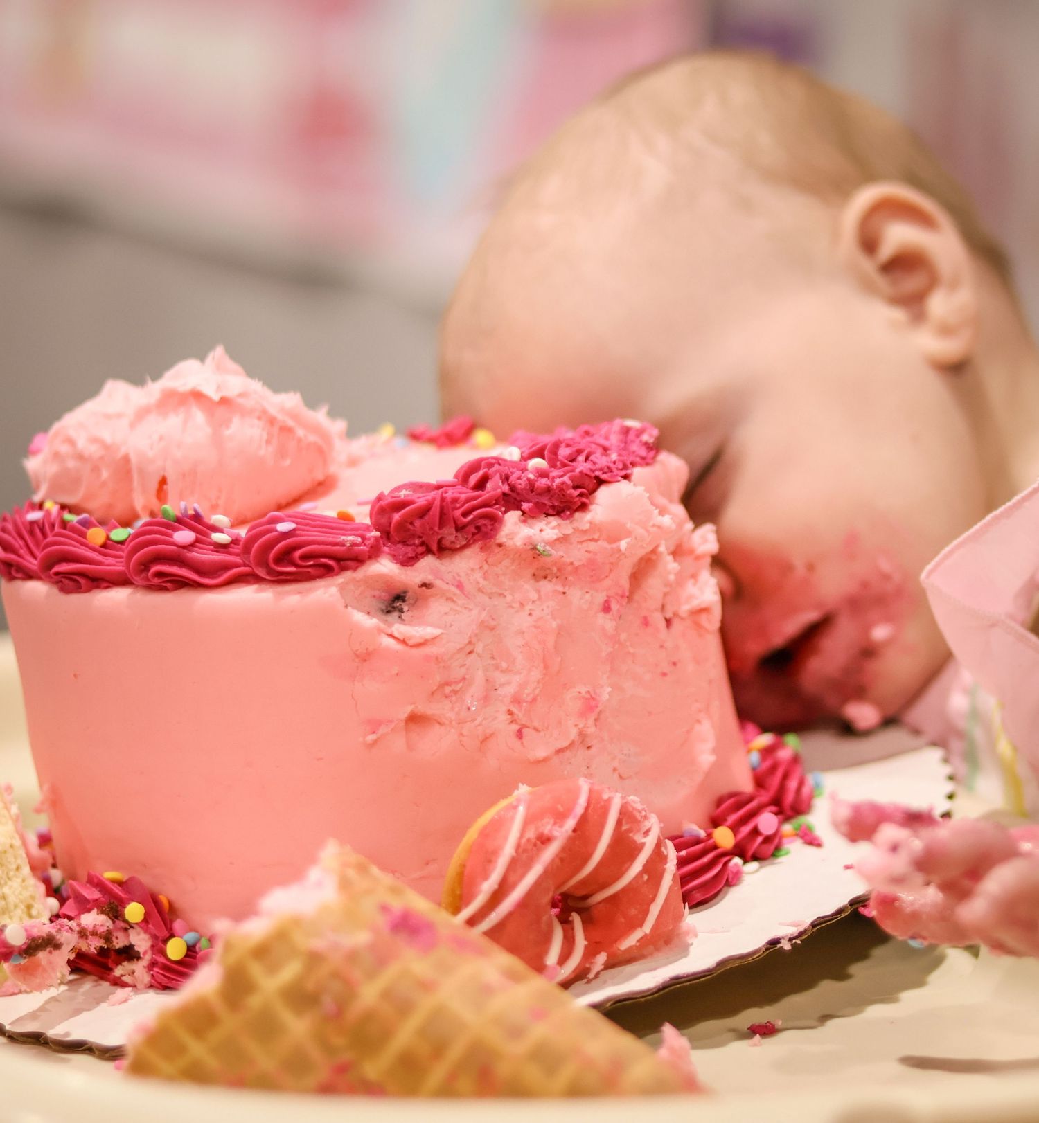 One year old girl falls asleep during cake smash. large pink cake is next to her