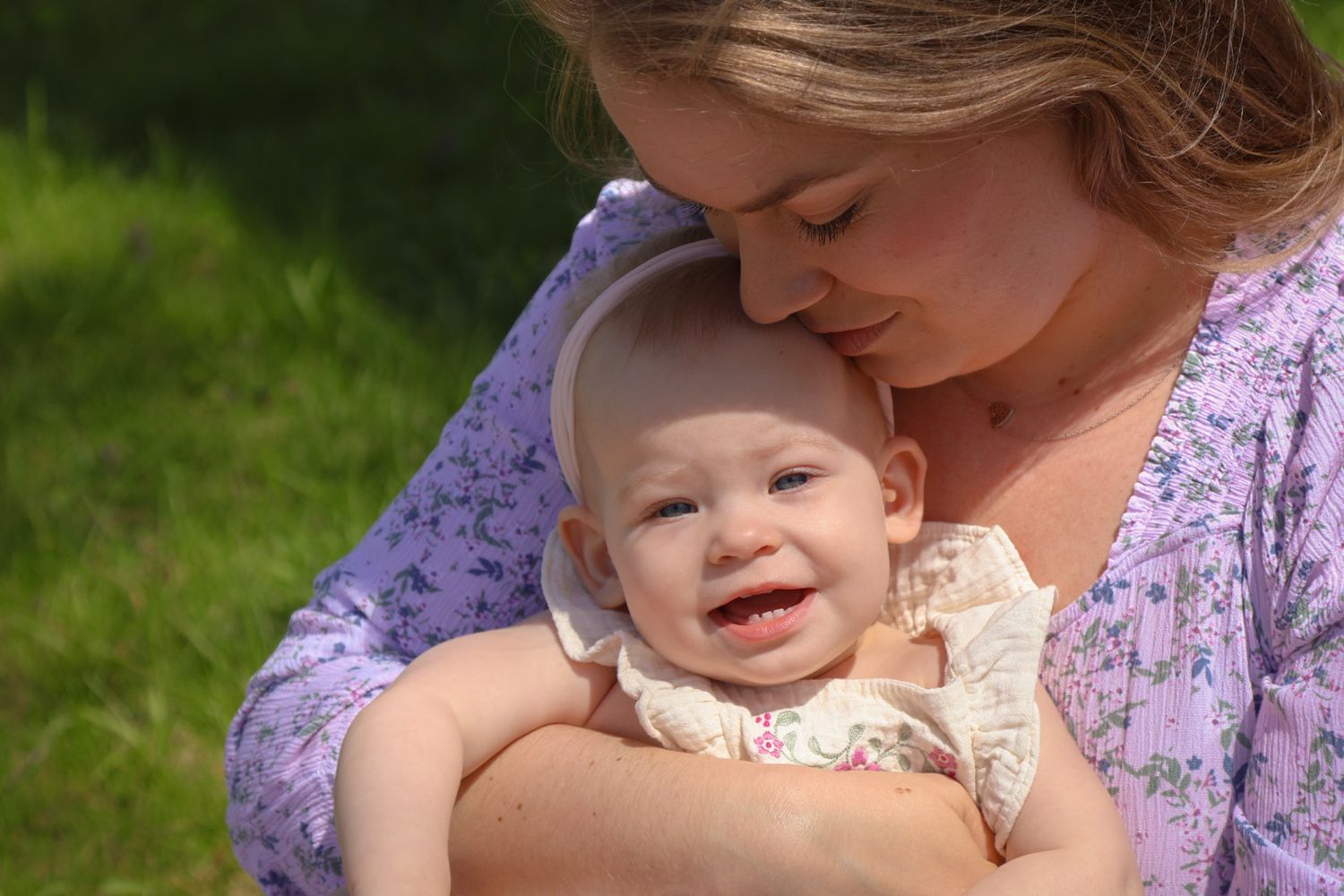 Mother cuddling baby daughter while they bask in the sunlight together on a warm spring day