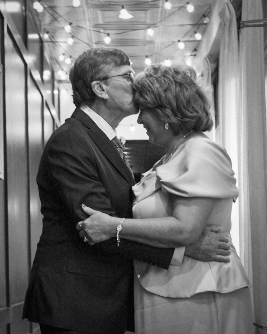 Groom kisses forehead of his bride with lights above their heads