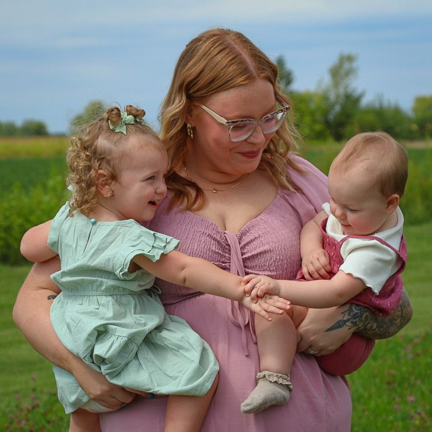 Mother holding two toddlers in a green field during an outdoor family photography session