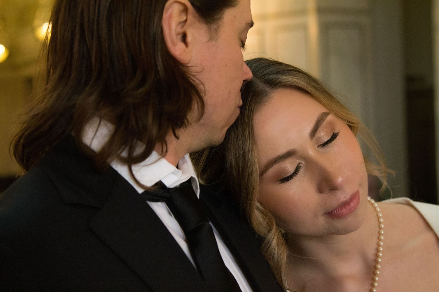Groom gently kissing his brides head as they both have calm expressions with closed eyes