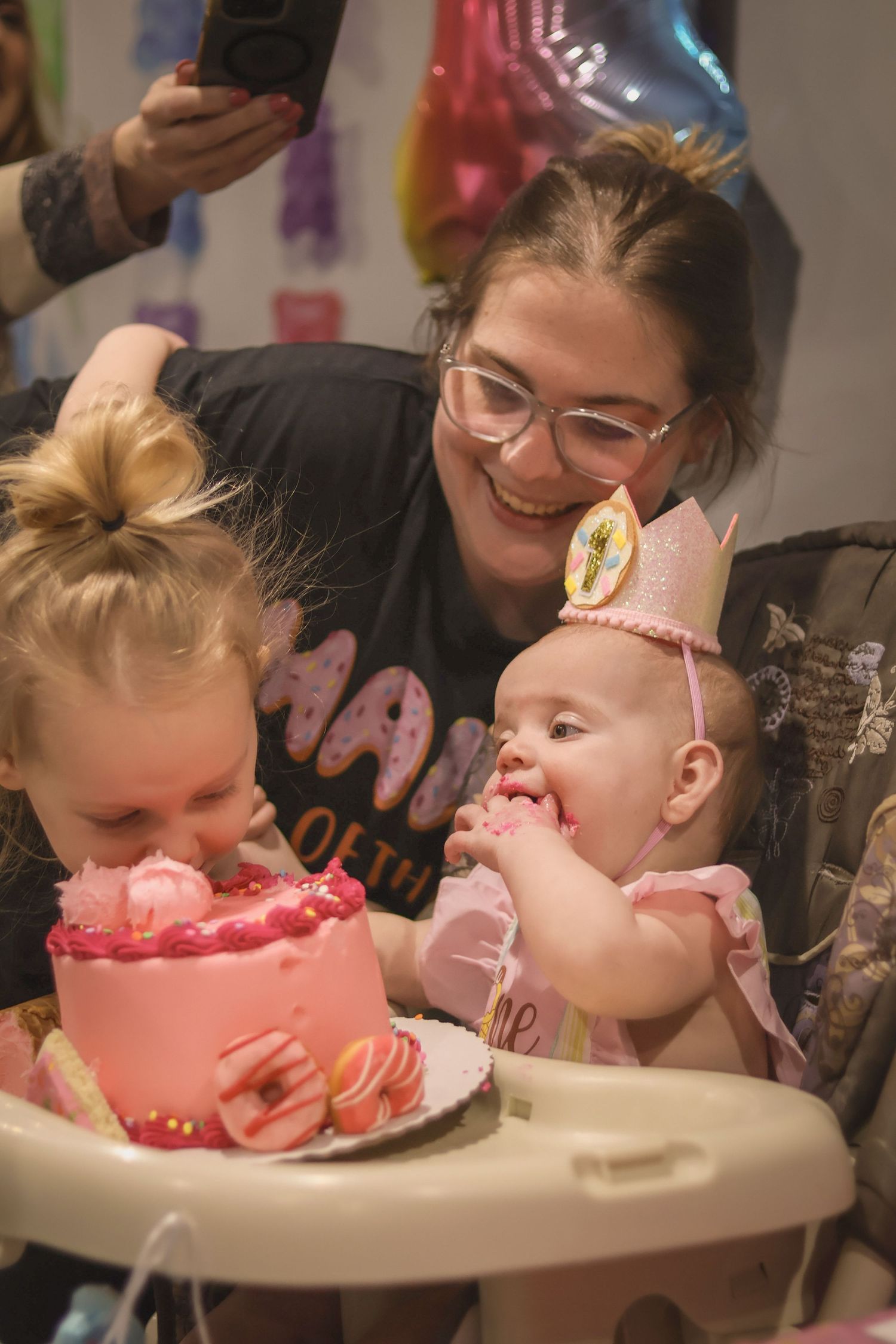 Mother is pictured with both daughters at birthday party as they huddle around the smash cake