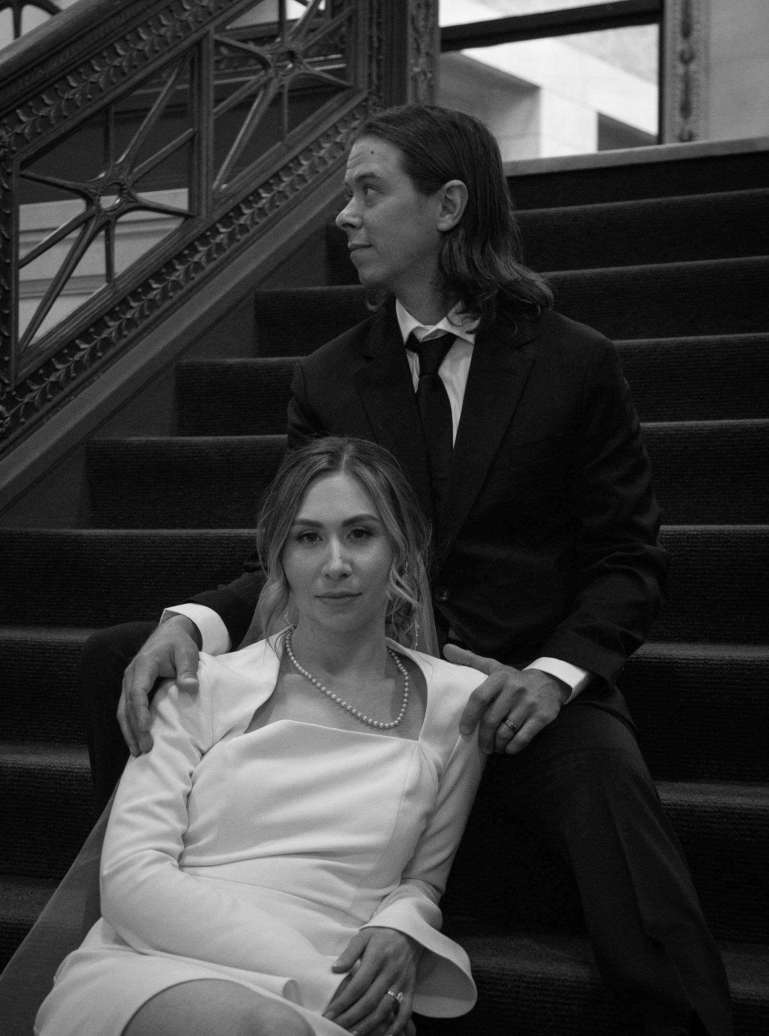 Bride and Groom pose on steps. Groom looks off while bride look at the camera with a gentle and beautiful look