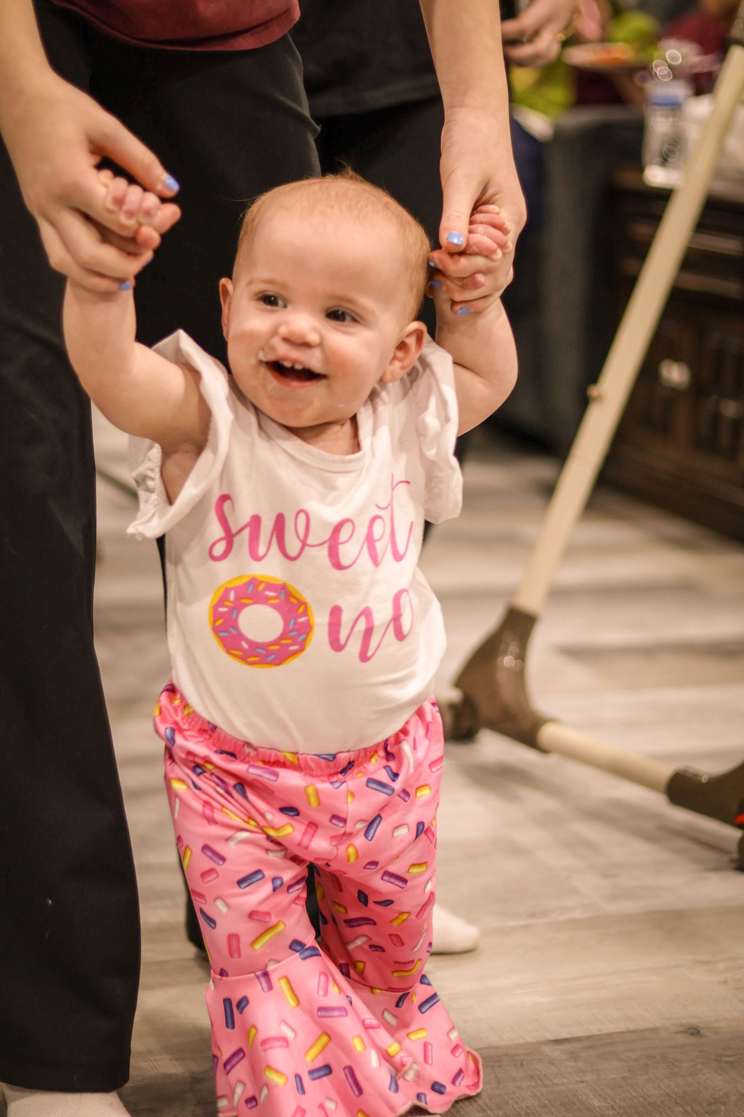 Baby in Sweet One outfit with pink sprinkle pants being walked by an adult