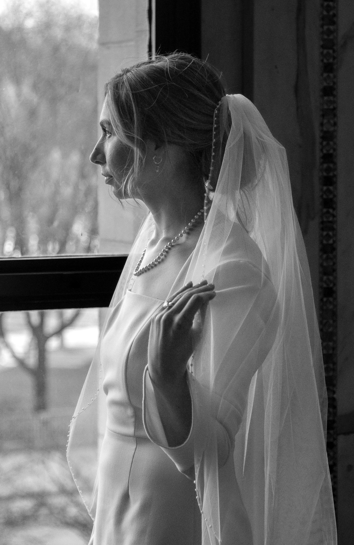 Bride portrait in black and white. Bride softly looks out the window of the Chicago Cultural Center and gently touches her veil