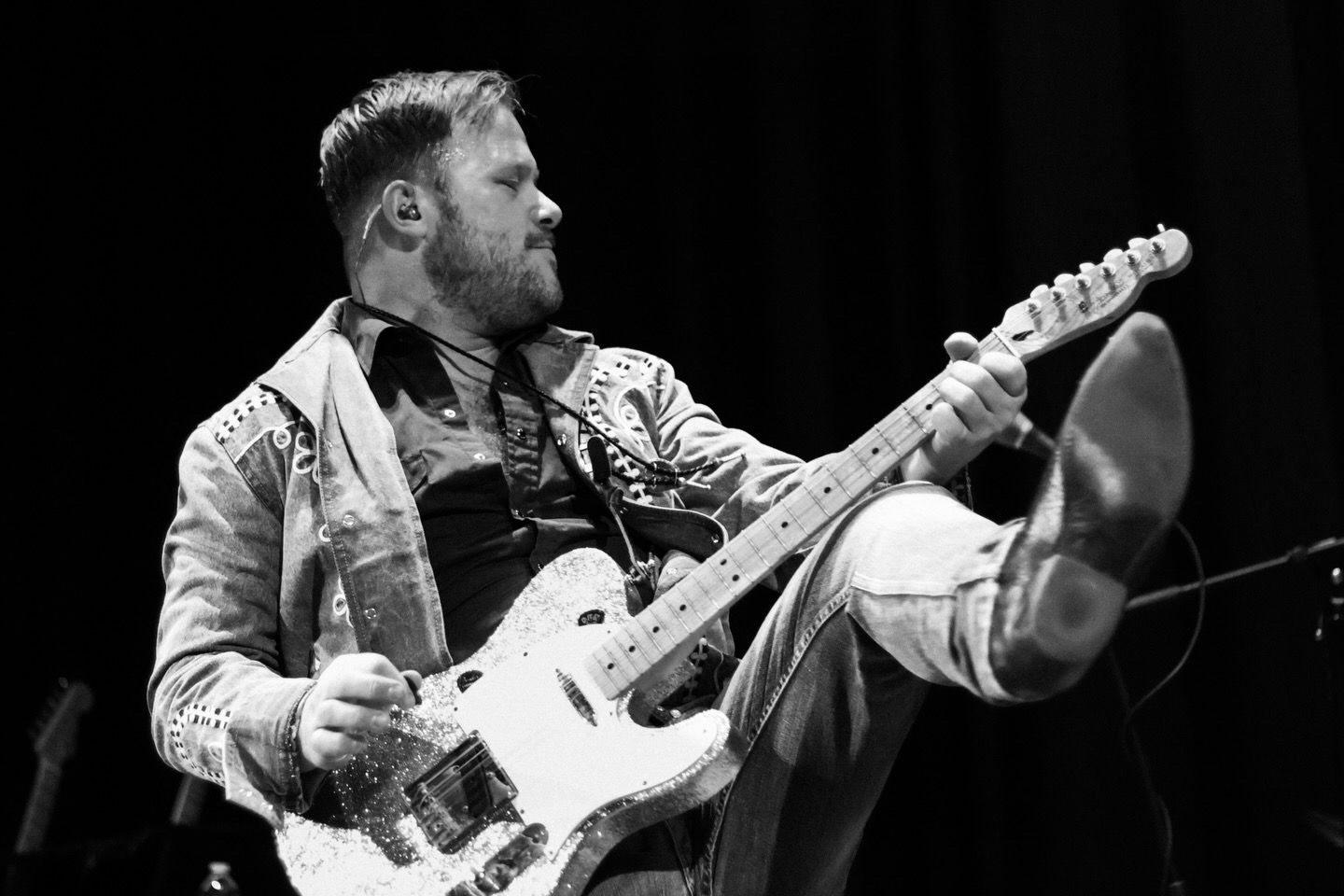 Lead singer and guitar player of the Band Iron Horse plays his guitar and kicks with lots of energy. Photo is black and white