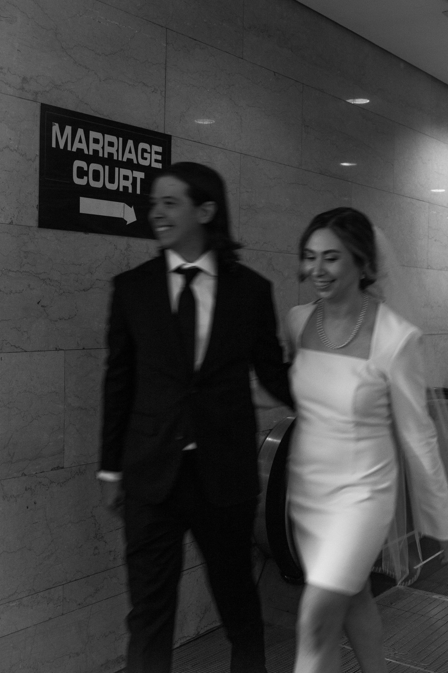 Bride and groom walk past marriage court sign at the chicago courthouse. photo is in black and white