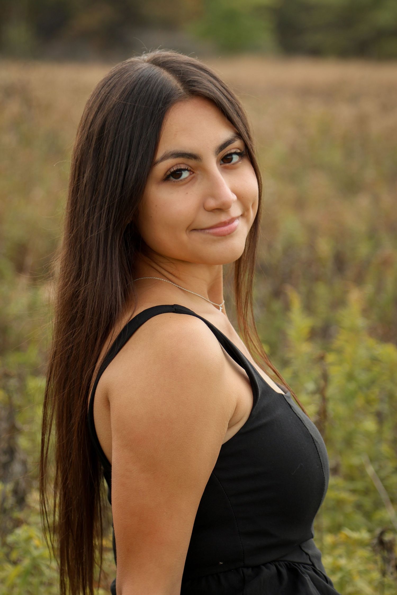Brunette senior smiles at camera in open field