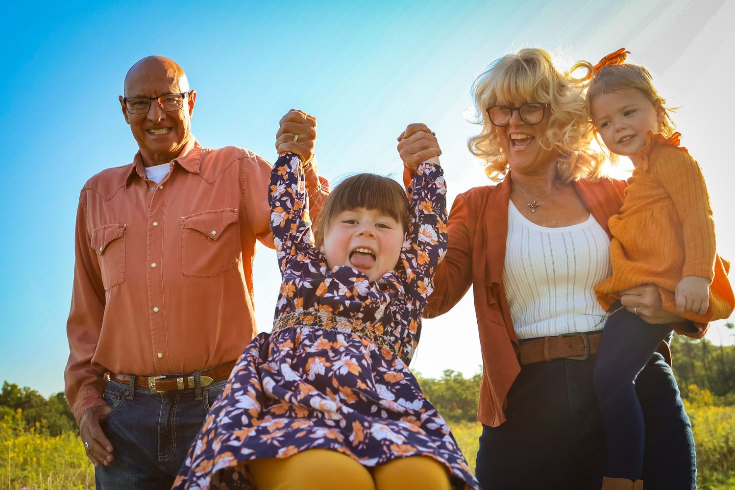 young girl playing with her grandparents and little sister as little girl is lifted up by them