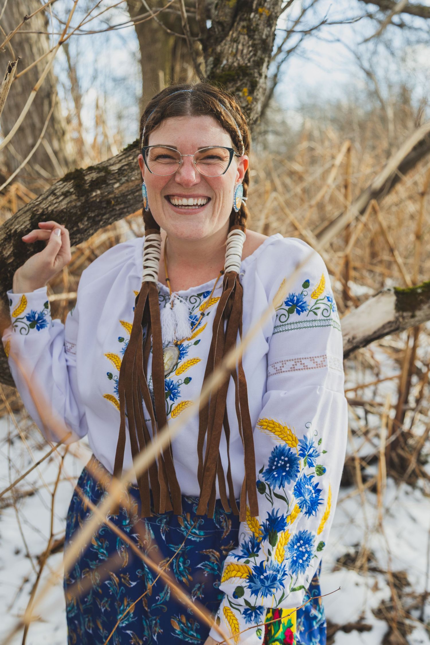 Smiling woman in embroidered Ukrainian vyshyvanka blouse with brown fringe necklace, standing outdoors in winter snow.