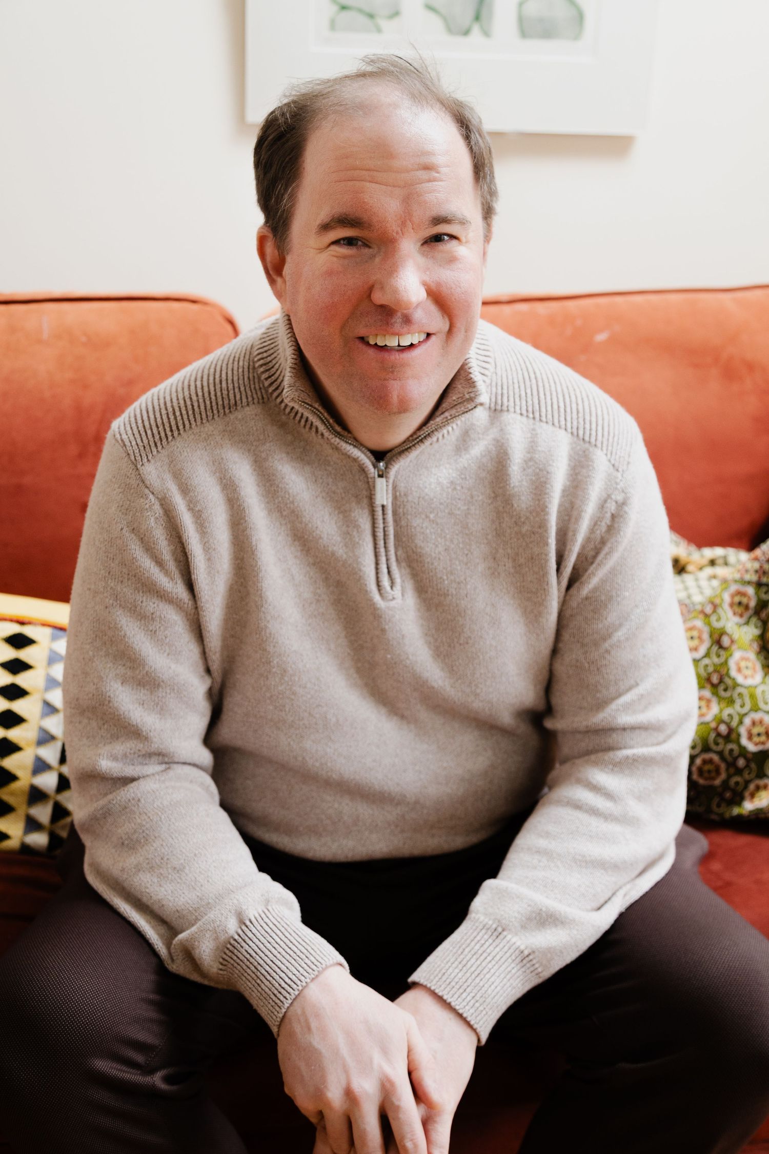 Casual indoor portrait on an orange couch wearing a beige quarter-zip sweater.