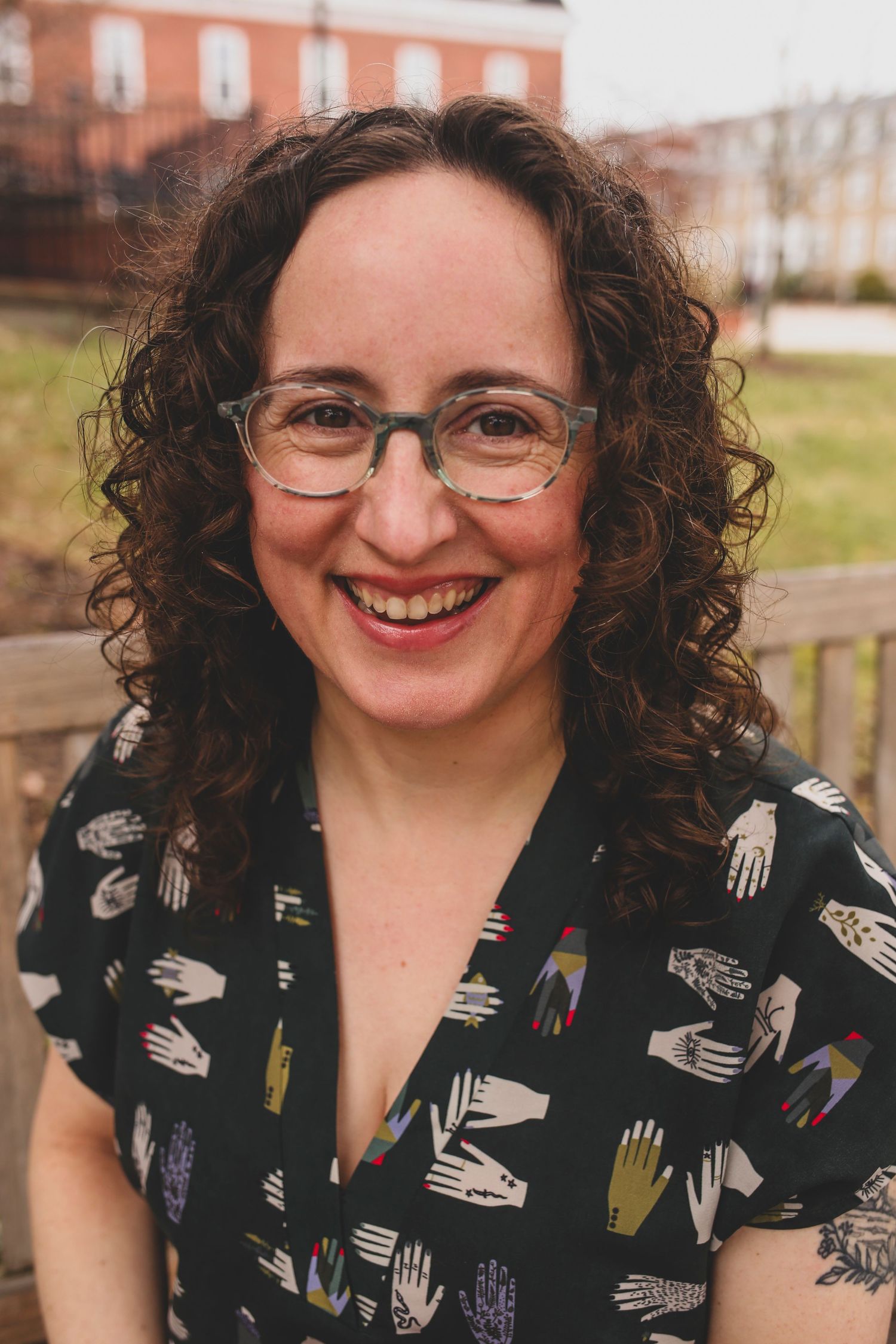 Portrait of someone in glasses and patterned shirt with hands design against brick building.