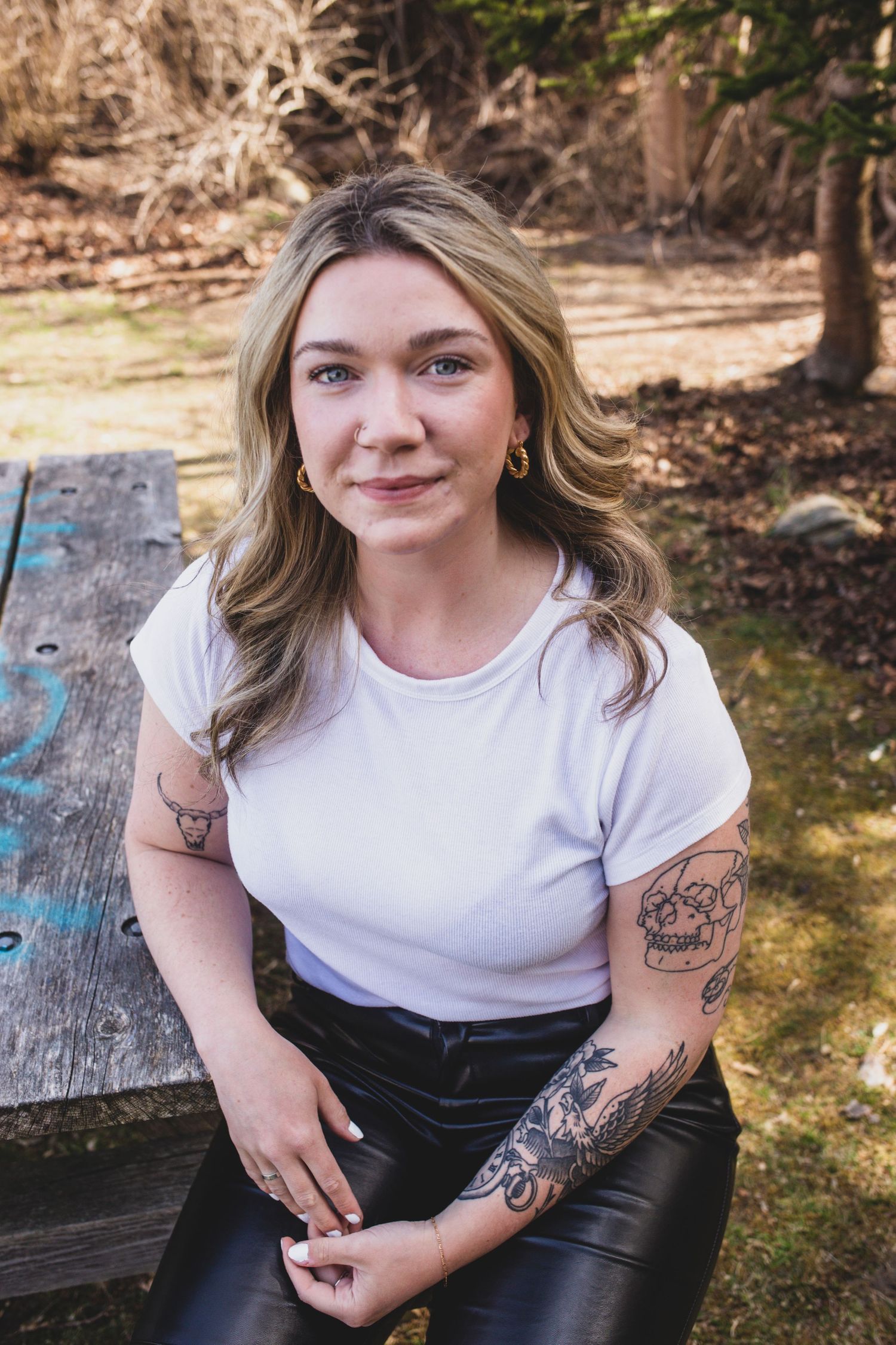 Casual outdoor portrait showing tattoo art while sitting on wooden bench in natural setting.
