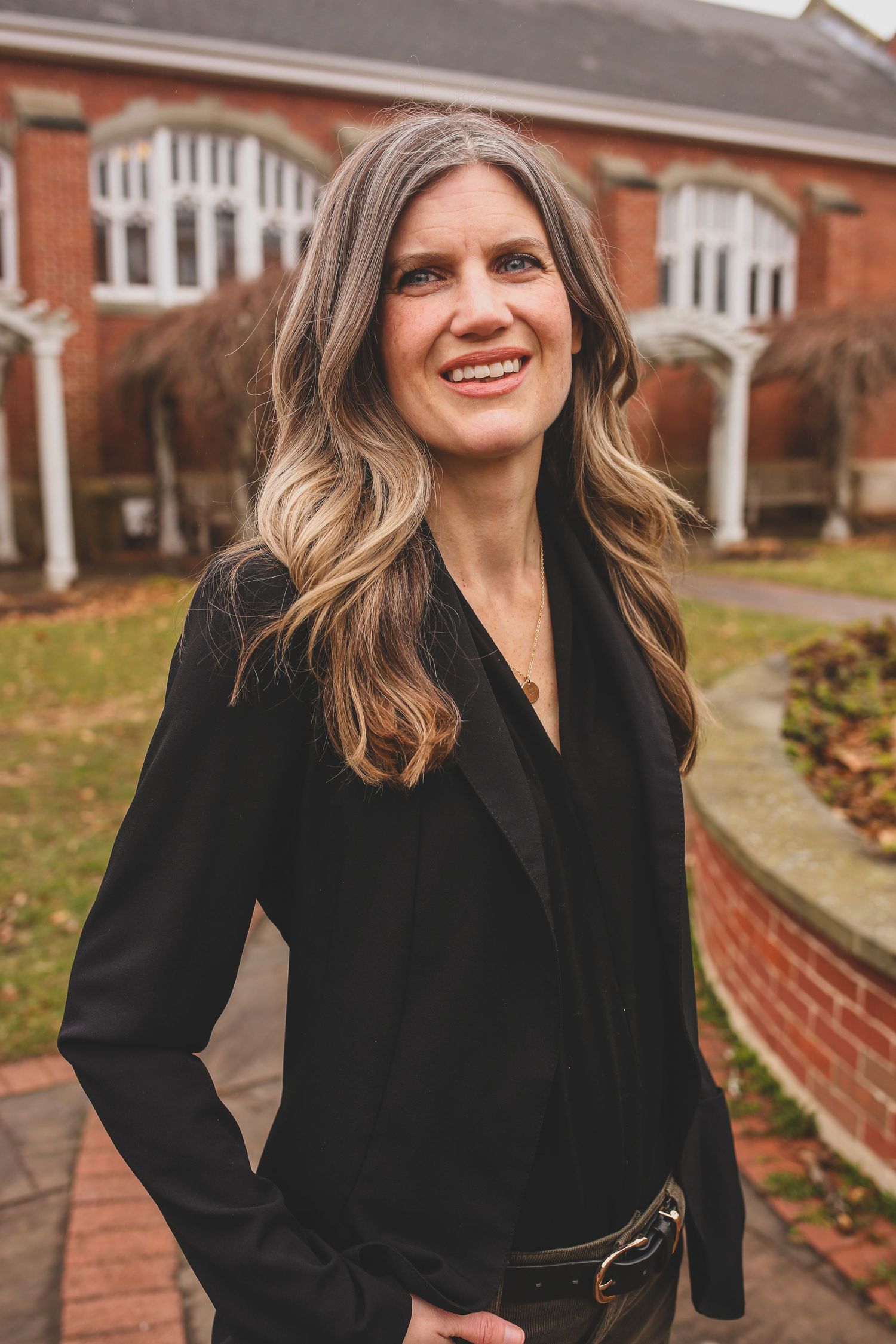 Professional outdoor portrait in black blazer with brick building and architectural details behind.