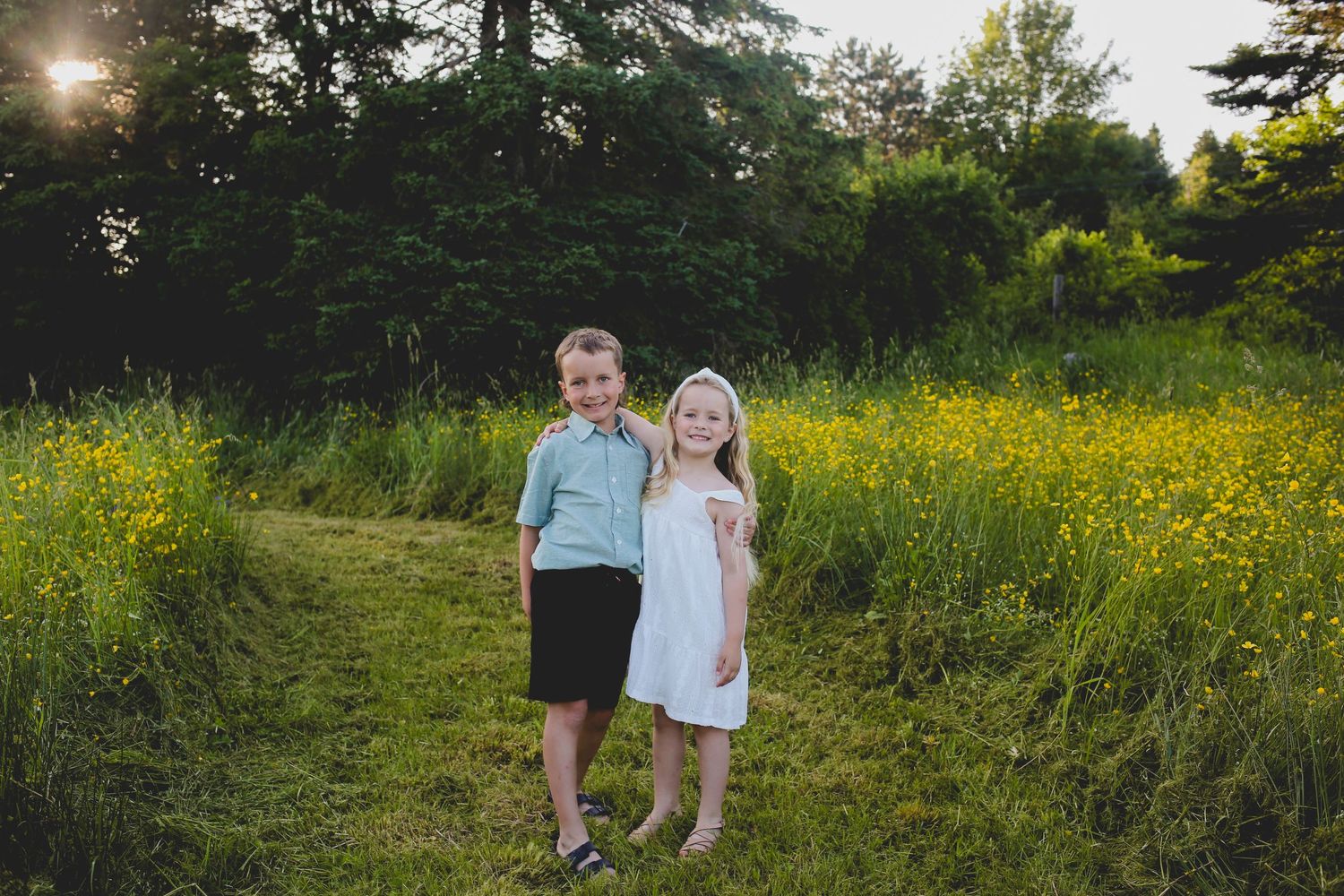 Couple walking through a golden wildflower meadow at sunset with tall trees in the background.