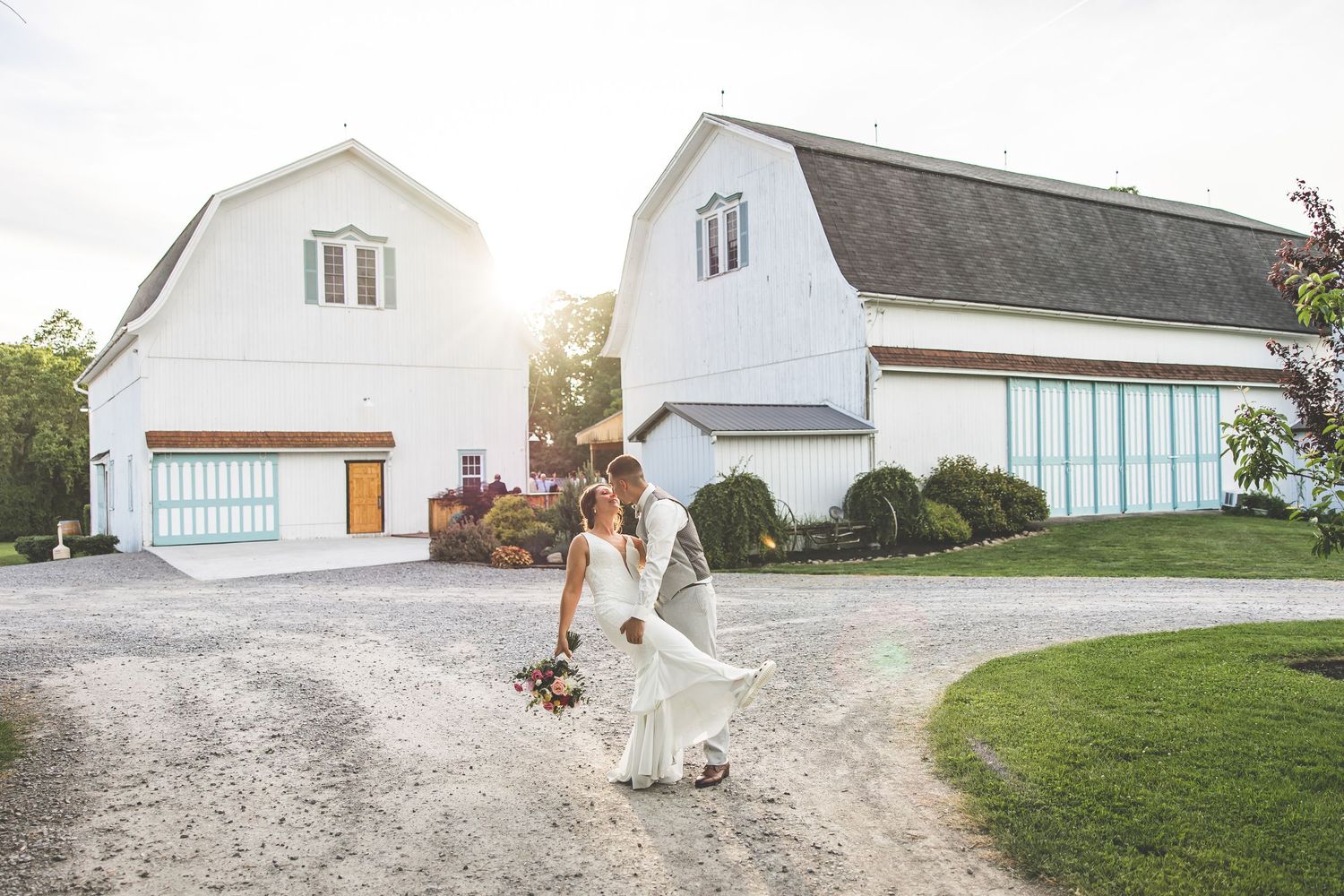 A white farmhouse and barn buildings with a gravel driveway at golden hour.