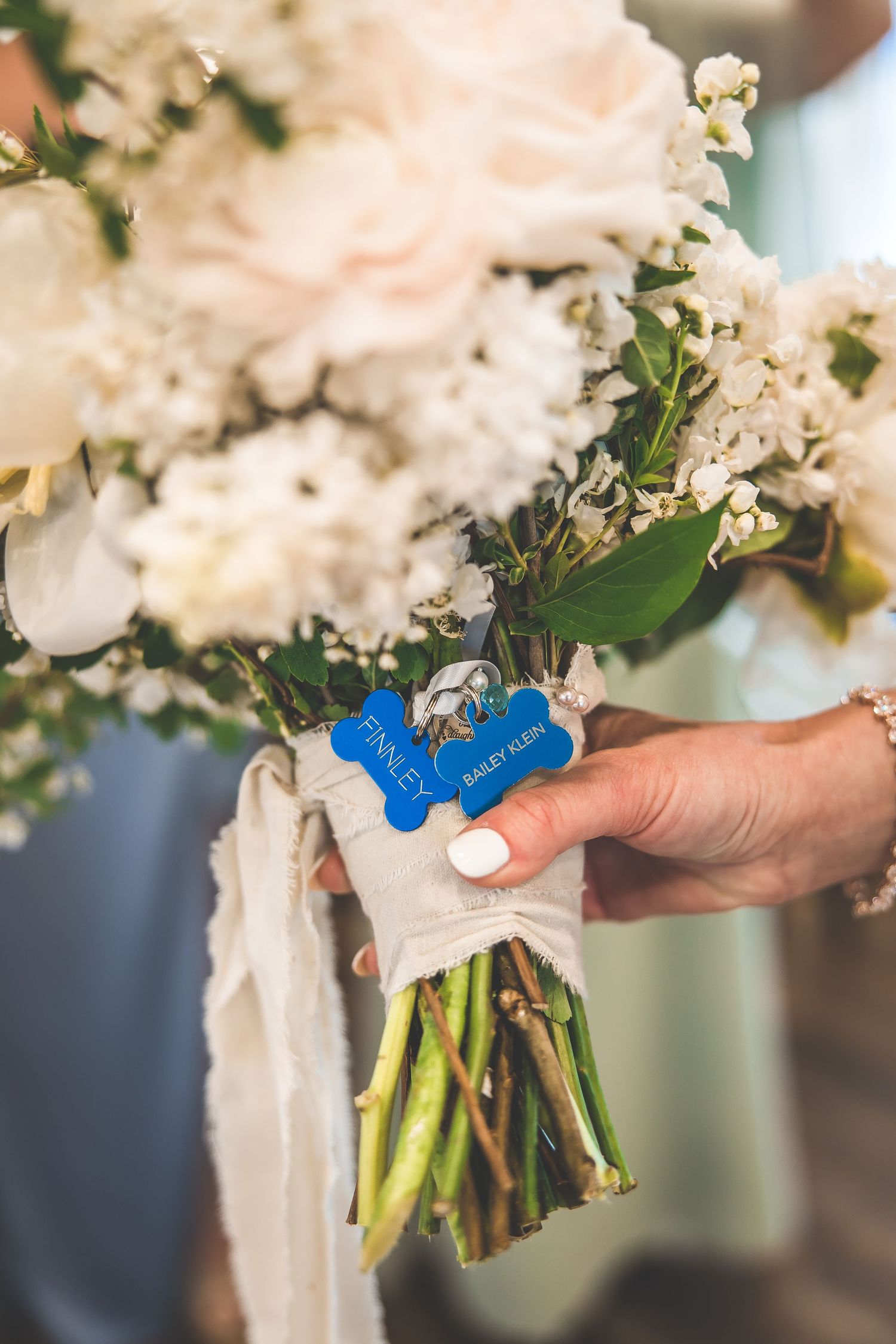 White floral bouquet with blue ribbon being held against a blurred background.