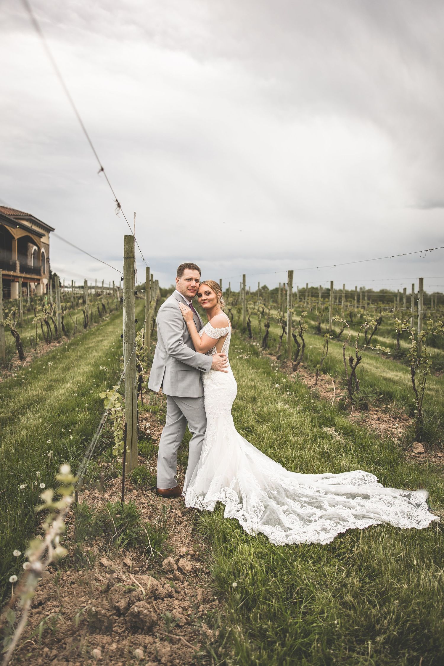 Wedding couple poses in a rustic vineyard setting with string lights overhead and flowing white dress.