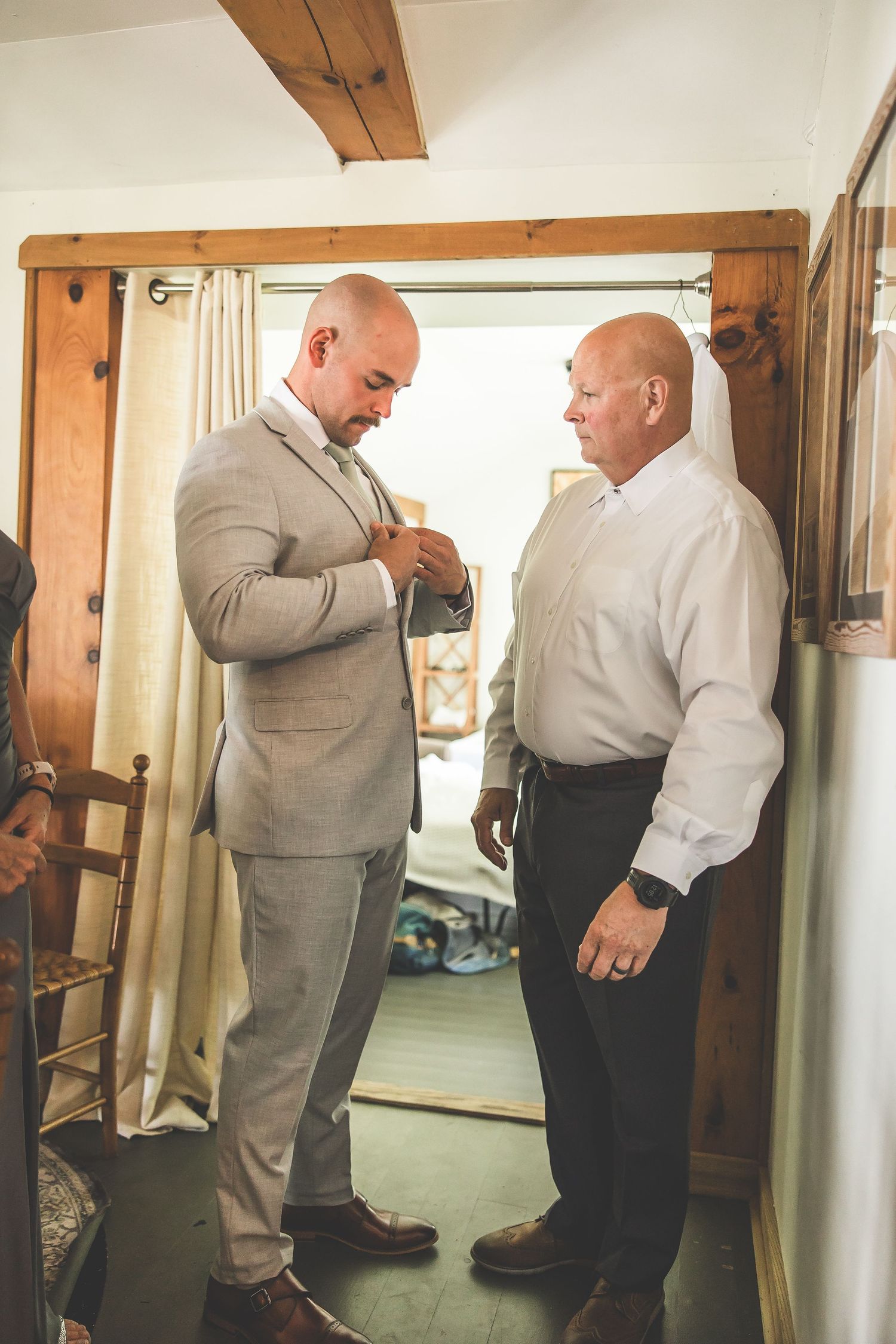 Men in formal attire help each other prepare in a wood-paneled dressing room.