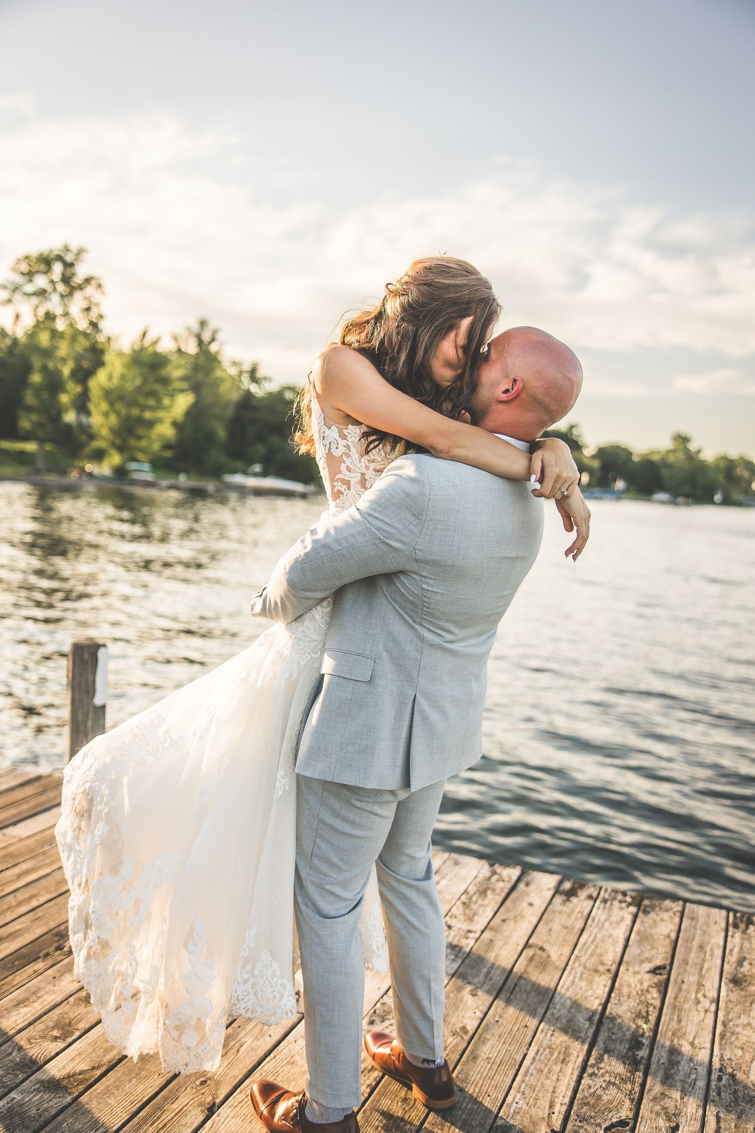 Romantic embraces captured on lakeside dock during wedding photoshoot.