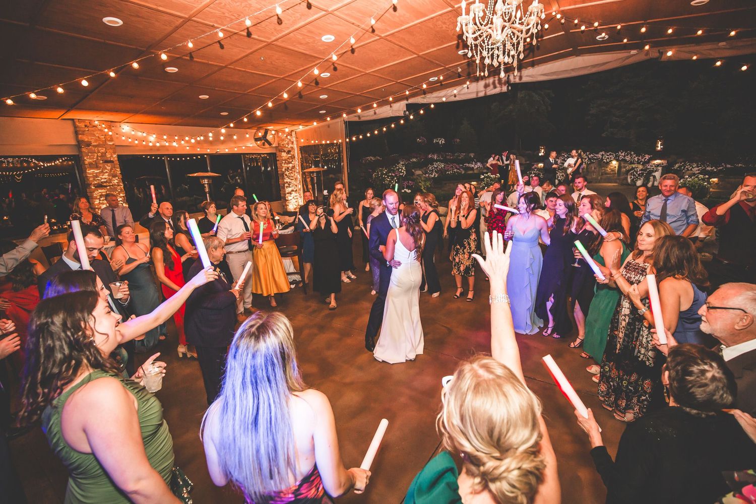 Wedding reception dance party with colorful lighting and chandelier in an elegant venue.
